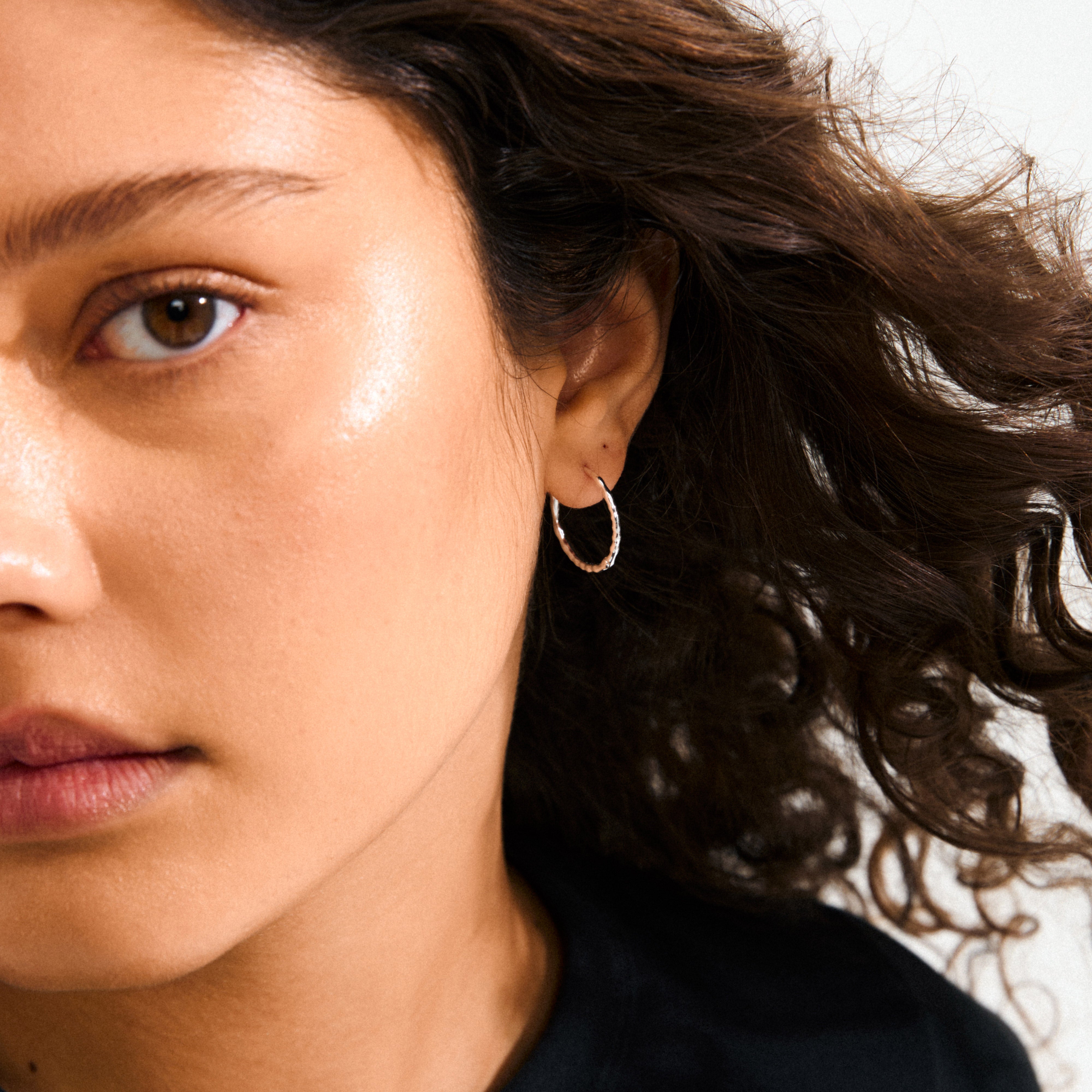 Close-up of a woman's face showcasing silver-plated BETWEEN hoops with an organic, flowing design, embodying minimalist yet substantial style.