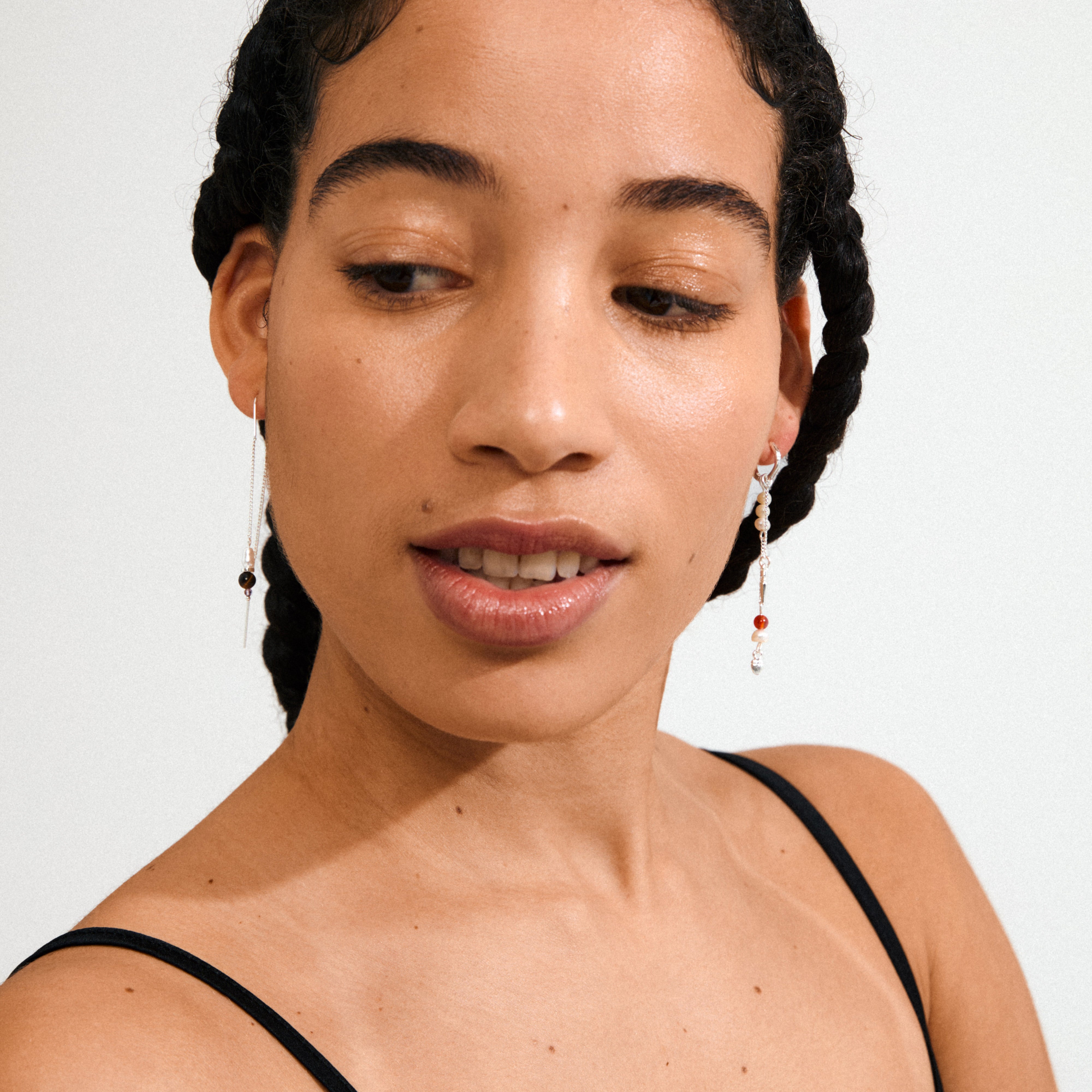 Close-up of lips and nose wearing Pilgrim's BETWEEN silver-plated chain earrings, featuring asymmetrical hoops with Amethyst, Aventurine, Tiger Eye, and pearl pendants.