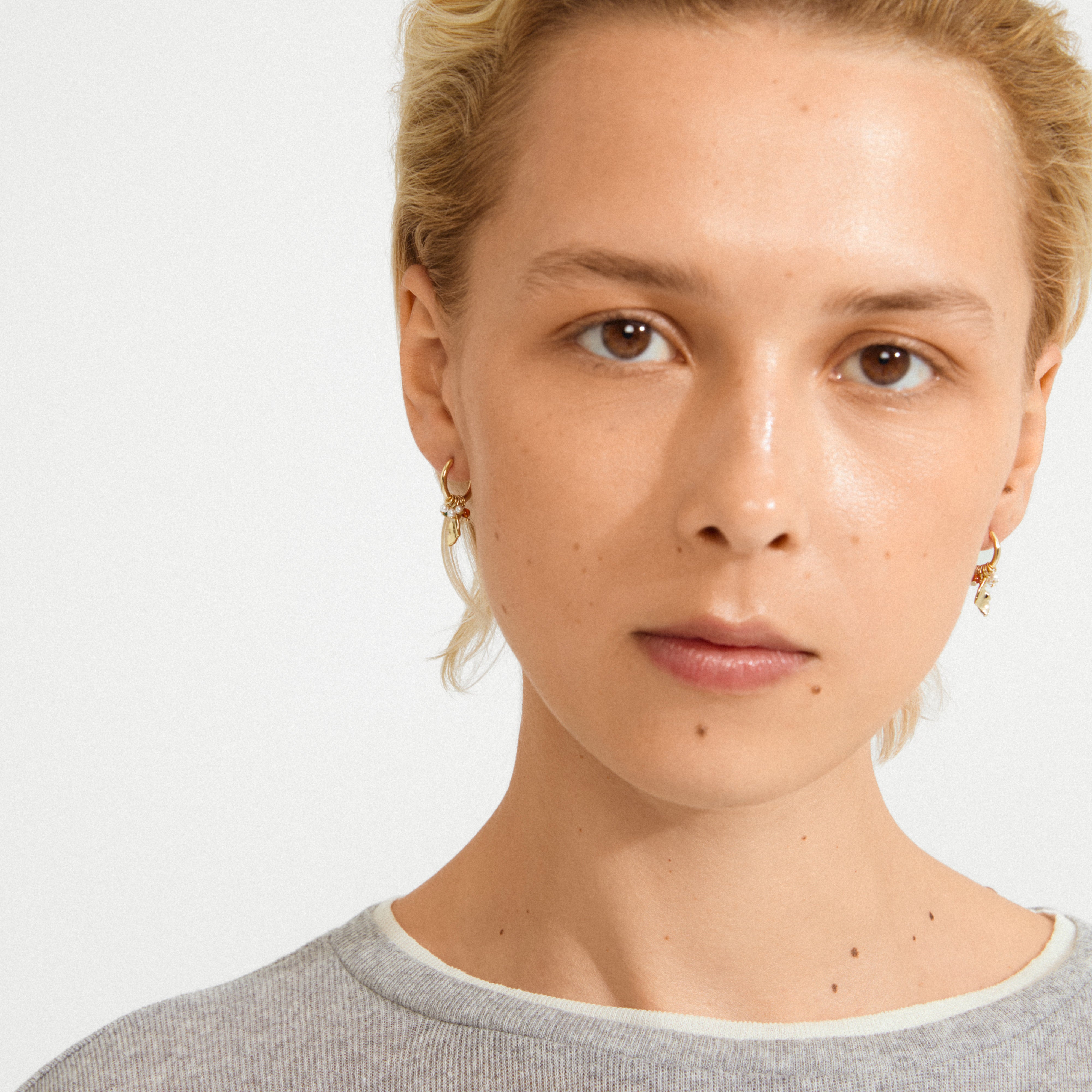 Person wearing Pilgrim's SENSE gold-plated huggie hoops with organic pendants, capturing a blend of boho-lux style in a simple portrait.