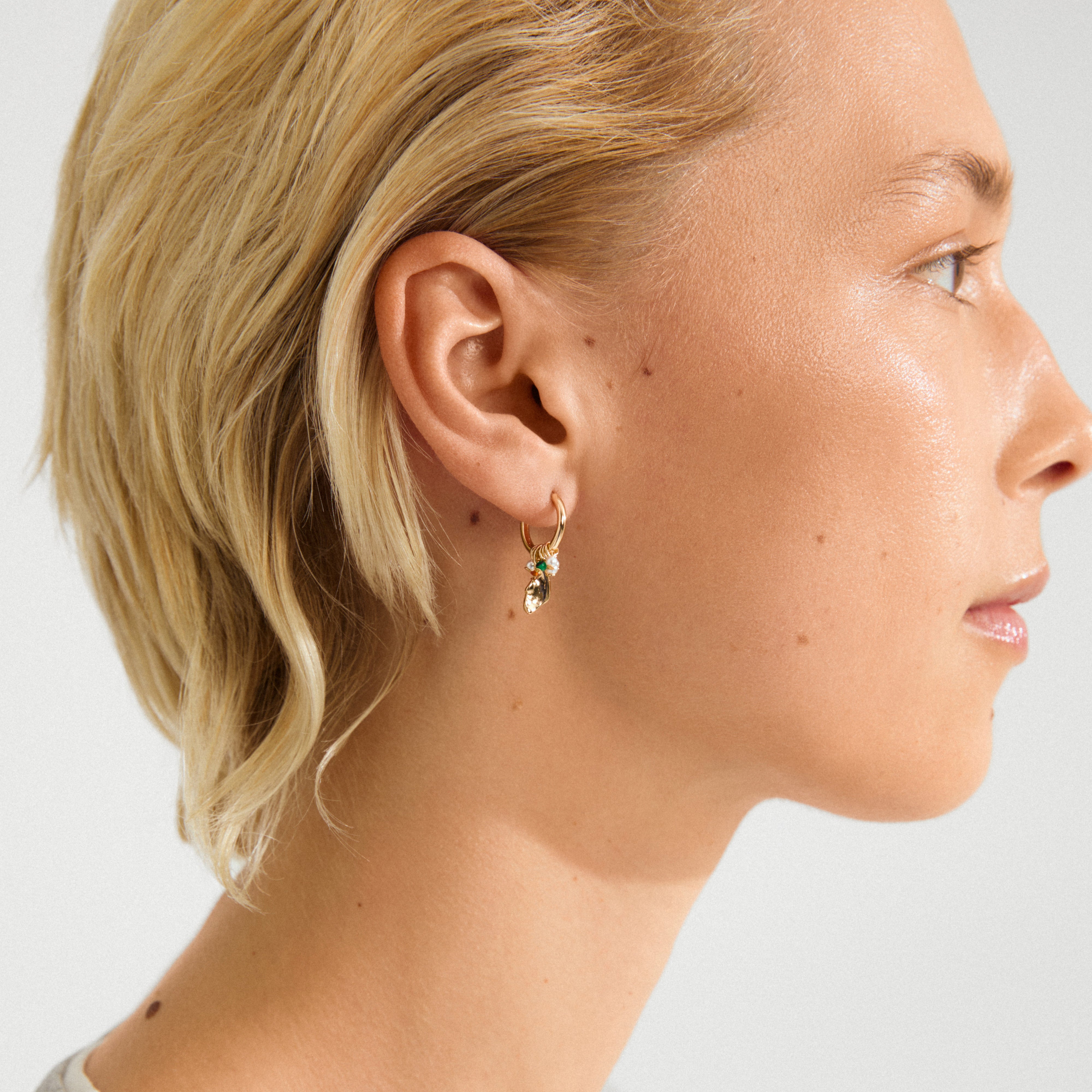 SENSE earrings gold-plated/multi feature a gold hoop with a leaf charm accented by a green stone, highlighting Pilgrim's boho-lux style and craftsmanship.