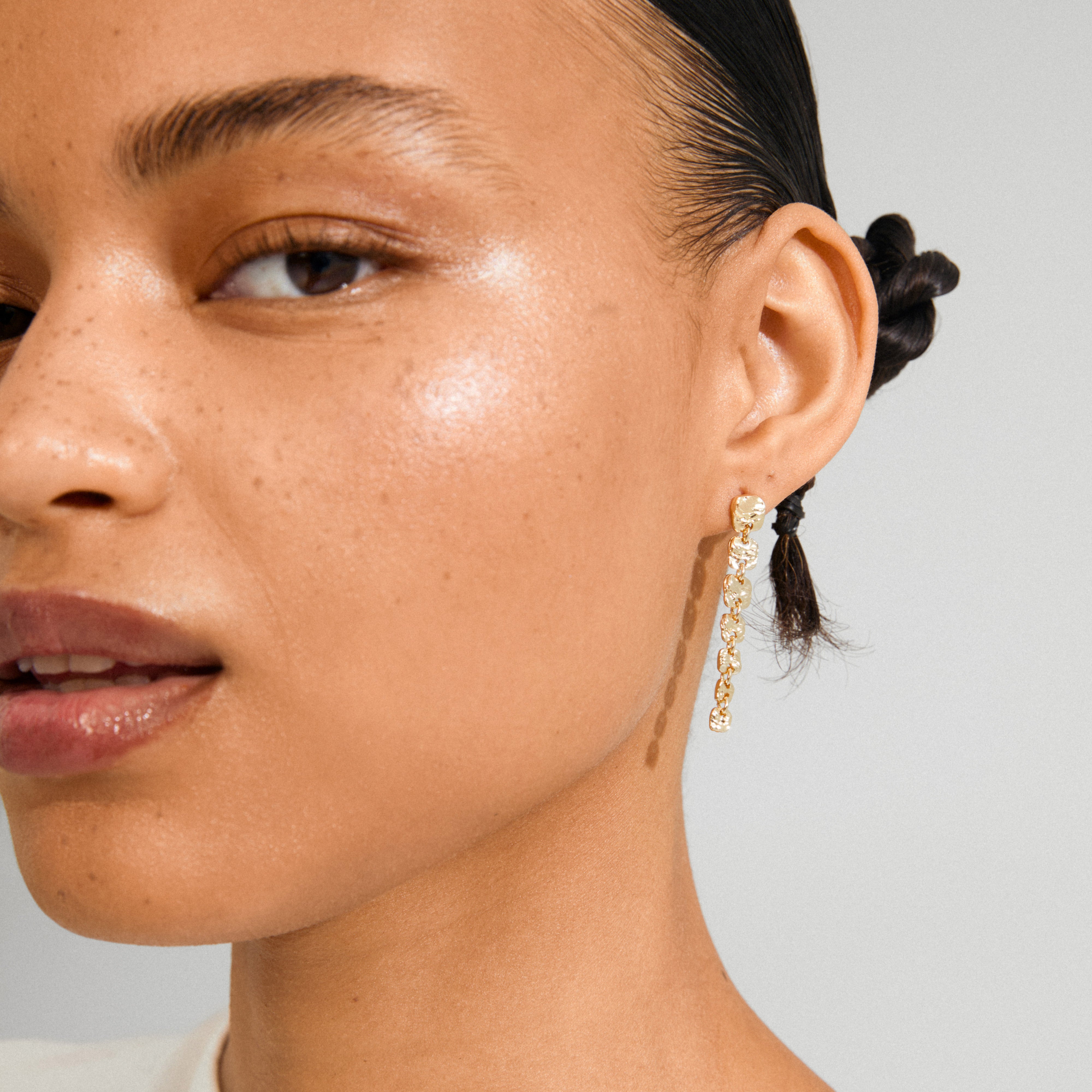 Close-up of SENSE earrings by Pilgrim, featuring gold-plated, textured, irregularly shaped segments hanging elegantly from an earlobe.