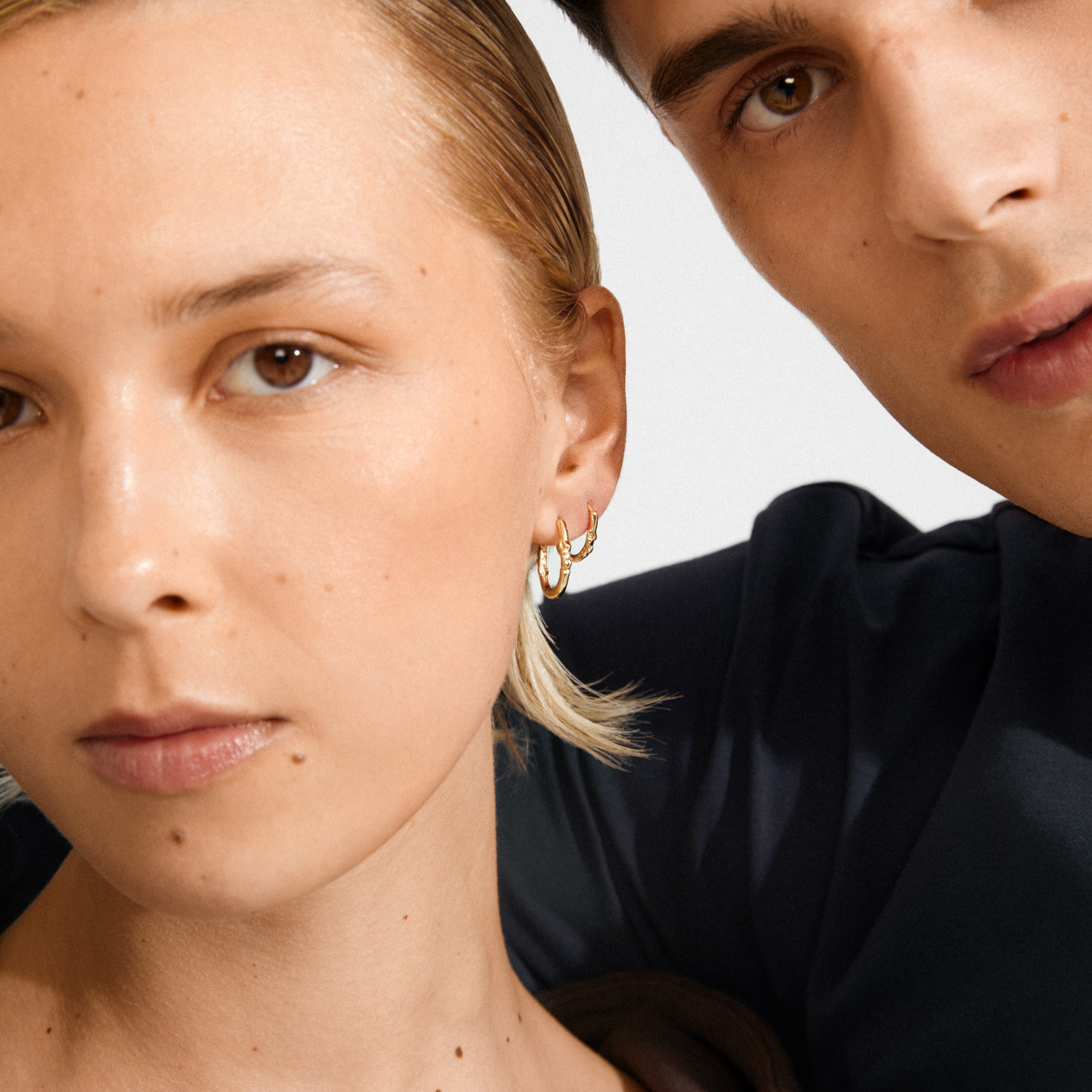 Two young adults showcase Pilgrim's SENSE hoop earrings, 2-in-1 gold-plated set, highlighting their organic design and versatile styling options.