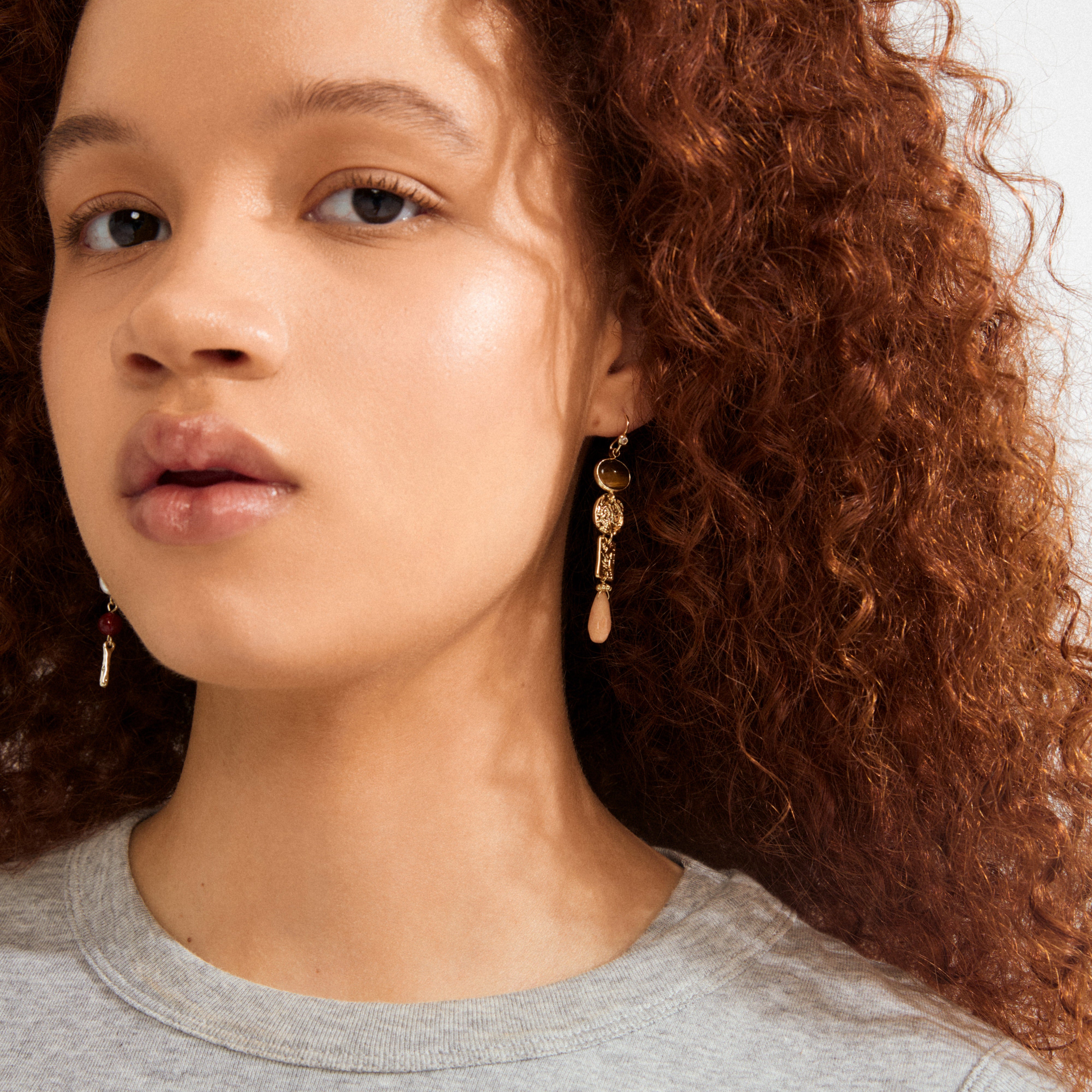 Young person wearing SENSE earrings gold-plated/multi by Pilgrim, featuring key-shaped charms and teardrop pendants, adding a boho chic vibe with colorful stones.