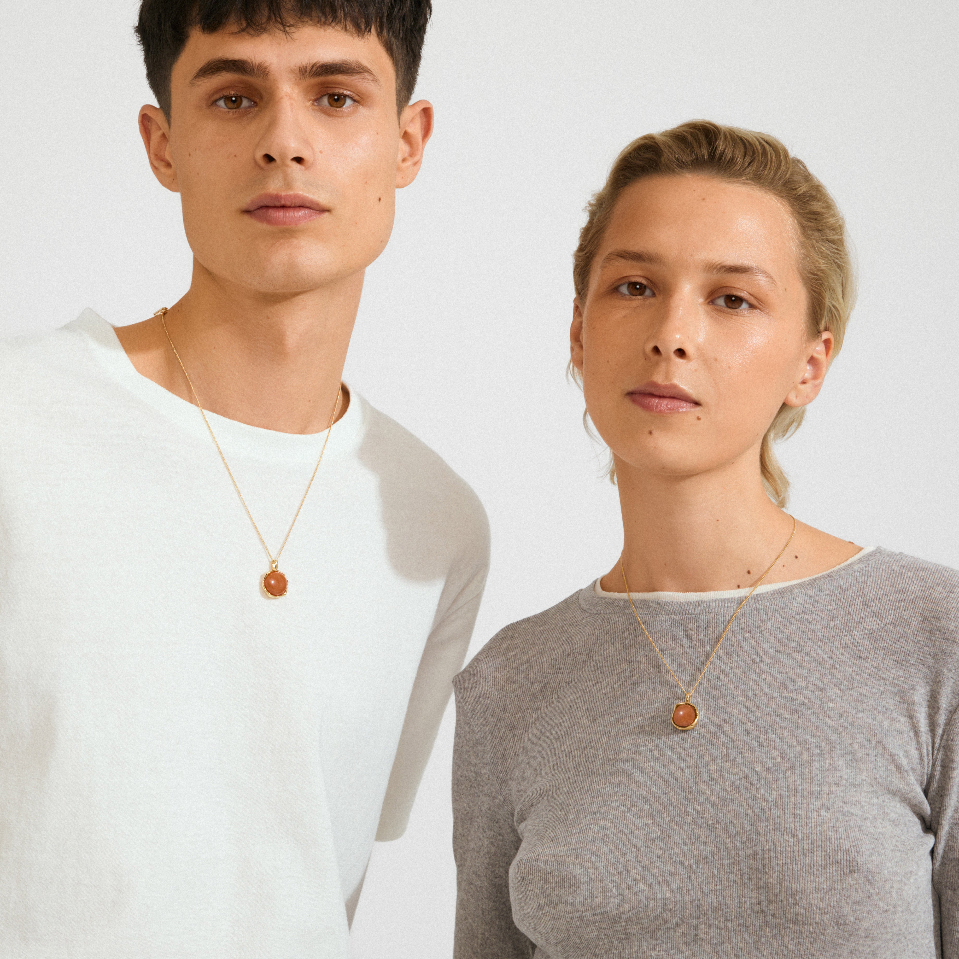 Two young adults showcase Pilgrim's SENSE necklace, featuring a gold-plated chain with a round Red Agate pendant, embodying strength and creativity.