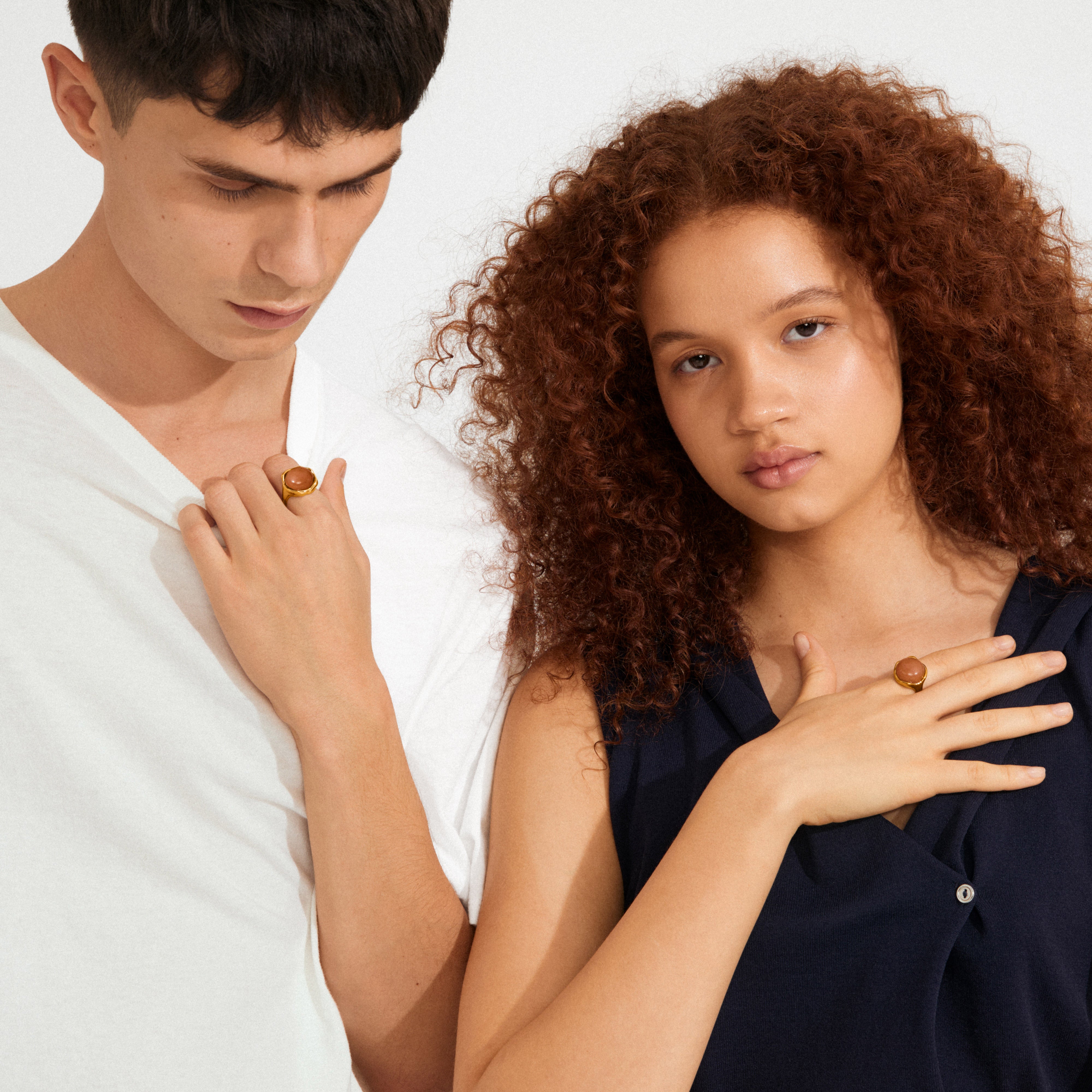 Two young people display Pilgrim's SENSE gold-plated agate rings, highlighting their sleek, minimalist design and organic beauty against a clean backdrop.