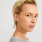 SENSE stud earrings silver-plated, worn by a person with short blond hair, showcase a rustic, wavy surface reflecting light for an effortlessly cool and stylish look.