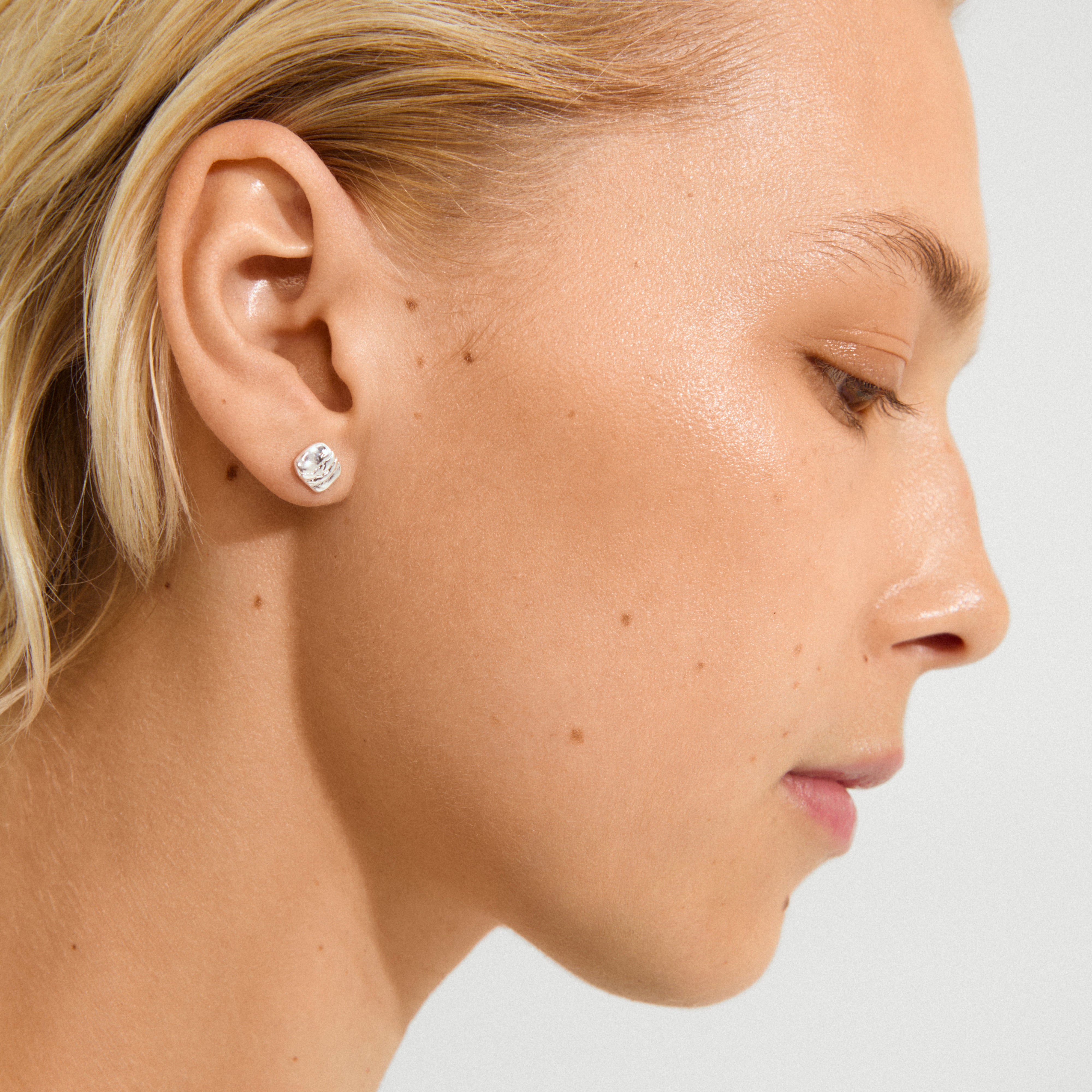 Side-profile of a person wearing Pilgrim's silver-plated SENSE stud earring with a wavy, light-reflecting surface, capturing a minimalist, effortlessly cool look.
