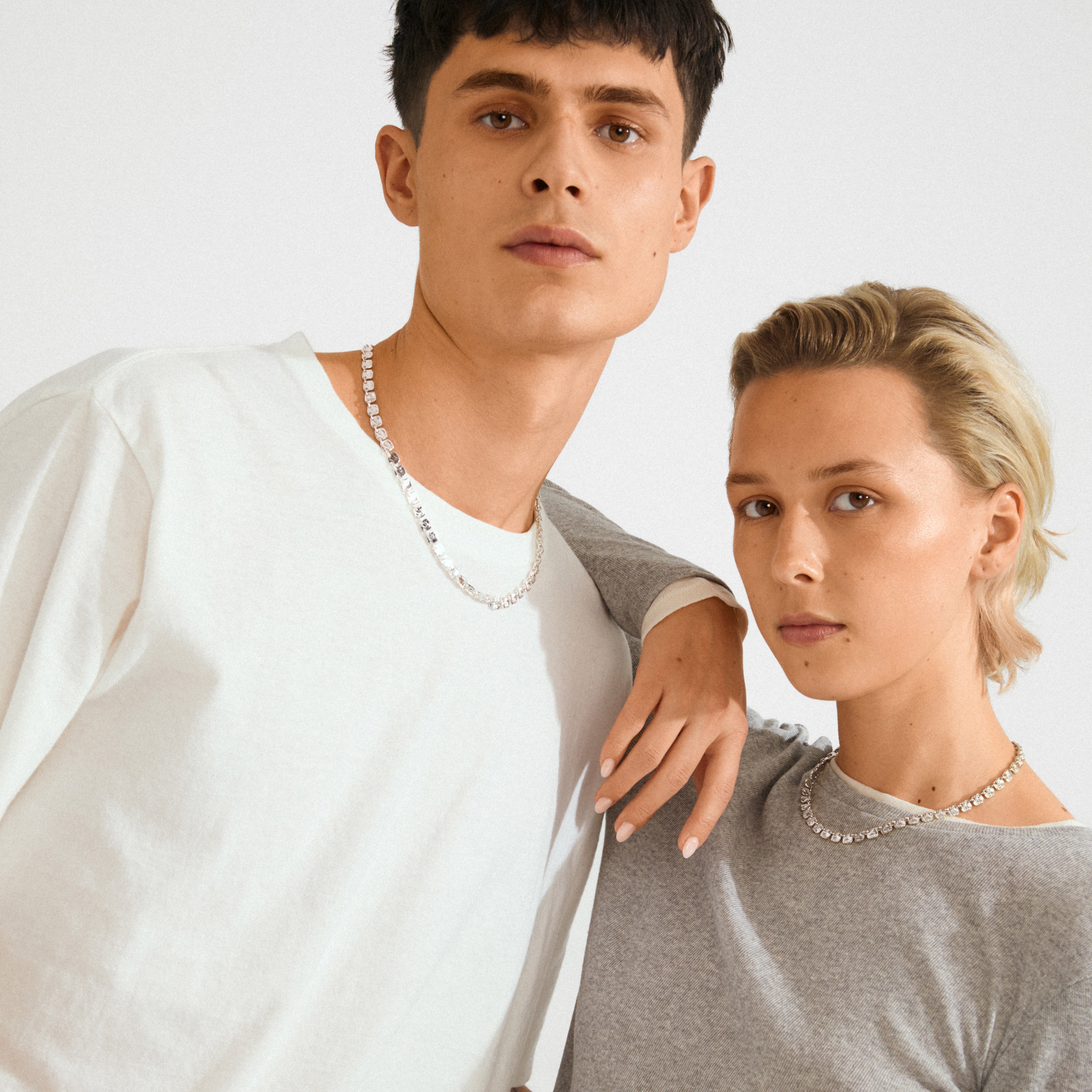 Two young adults showcasing Pilgrim's SENSE silver-plated necklace, featuring small square coins, embodying minimalist, modern style. Ideal for a versatile, everyday look.