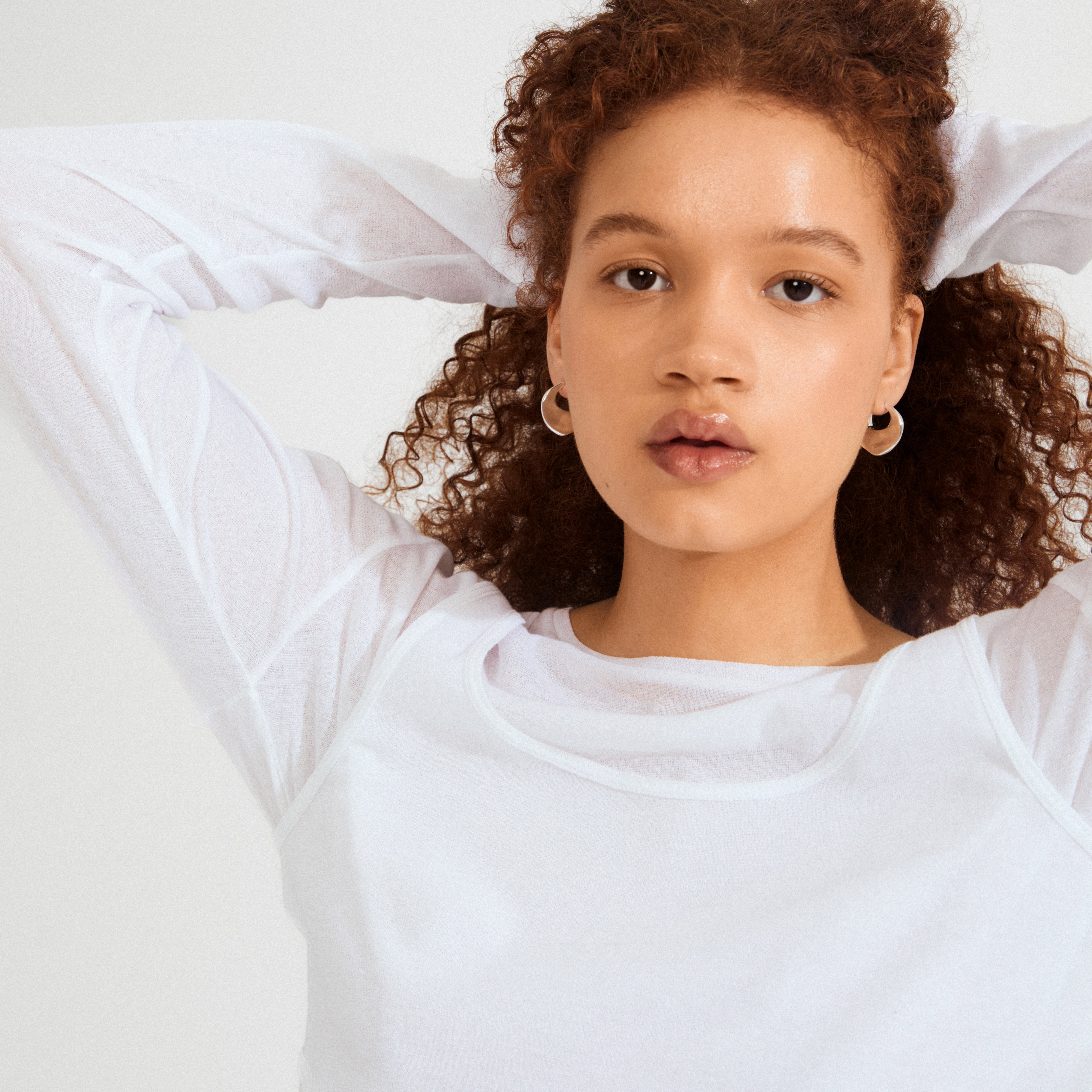 Young person wearing Pilgrim's SENSE hoop earrings, silver-plated with a wavy design, showcasing a minimal, stylish look against a light background.