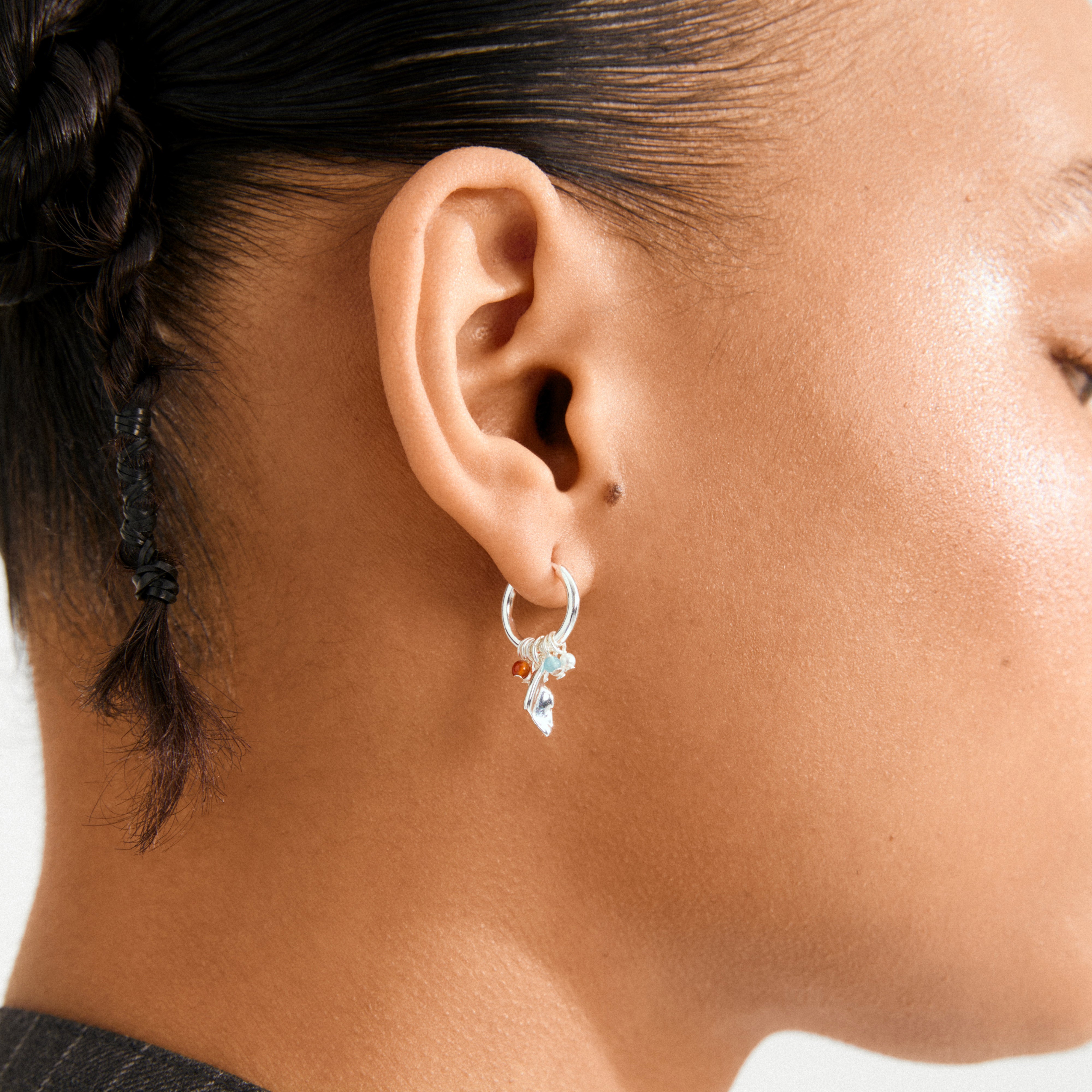 Close-up of an ear wearing Pilgrim's silver-plated SENSE huggie hoops with dangling charms and beads, showcasing a trendy, free-spirited style.