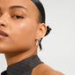 Close-up of a face wearing SENSE earrings silver-plated/multi, showcasing a delicate silver hoop with a dangling charm, paired with a high-collared, dark gray top.