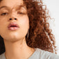 Close-up of SENSE earrings silver-plated by Pilgrim, featuring a dangling silver earring on a person with glossy lips and long, curly reddish-brown hair.