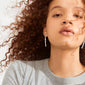 Young person wearing SENSE earrings, silver-plated with movable crystal drops, reflecting light. The focus is on their neck and pensive expression, highlighting the earrings' dynamic design.