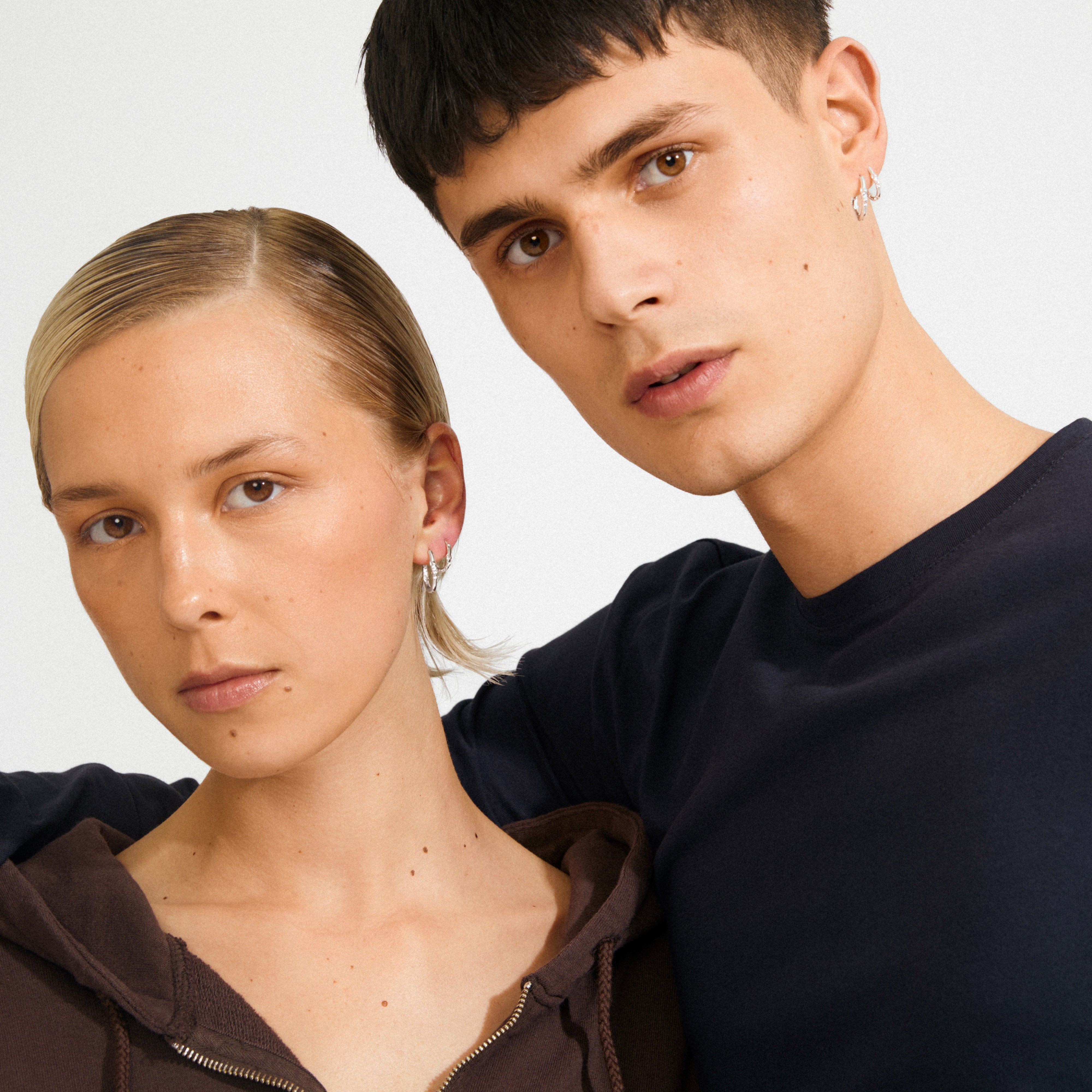 Two young adults wear SENSE hoop earrings, 2-in-1 silver-plated, showcasing minimalist elegance and versatile style from Pilgrim.