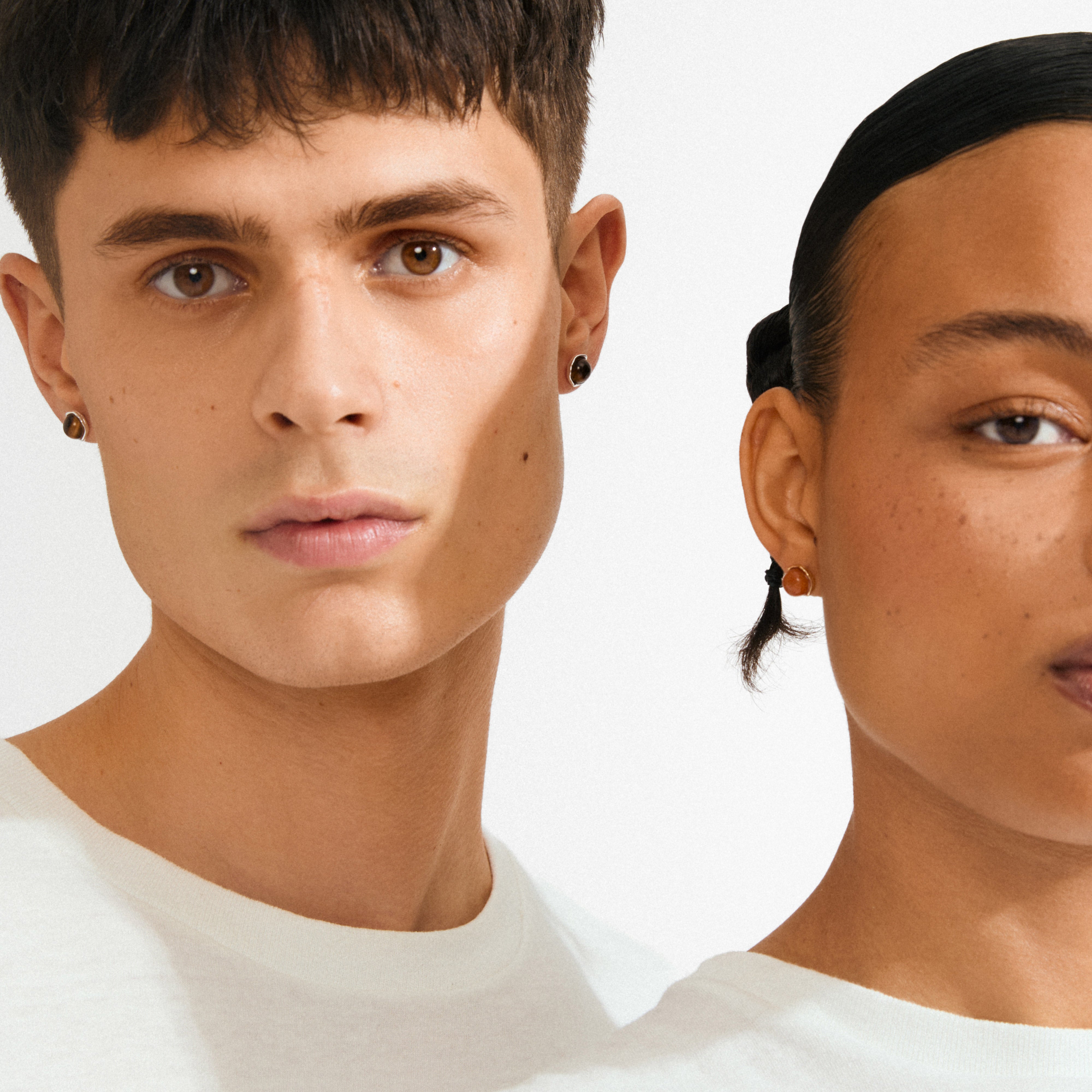 Two young adults wearing Pilgrim's SENSE earrings, featuring silver-plated settings with Tiger Eye stones, symbolizing strength and balance. Perfect for minimalist or stacked styles.