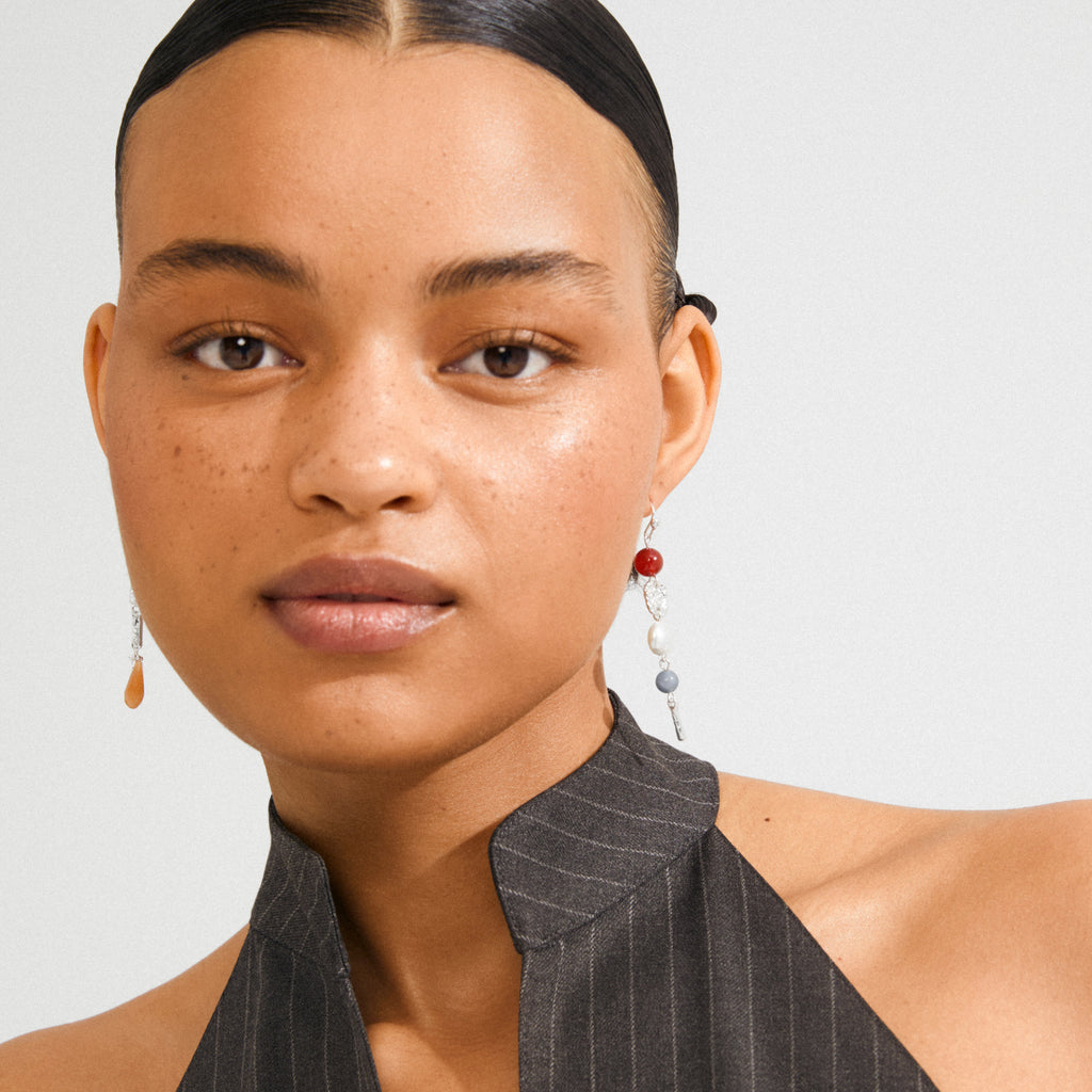 Young woman wearing Pilgrim's SENSE earrings, featuring asymmetrical silver-plated drops with colorful beads, highlighting a boho luxe style.