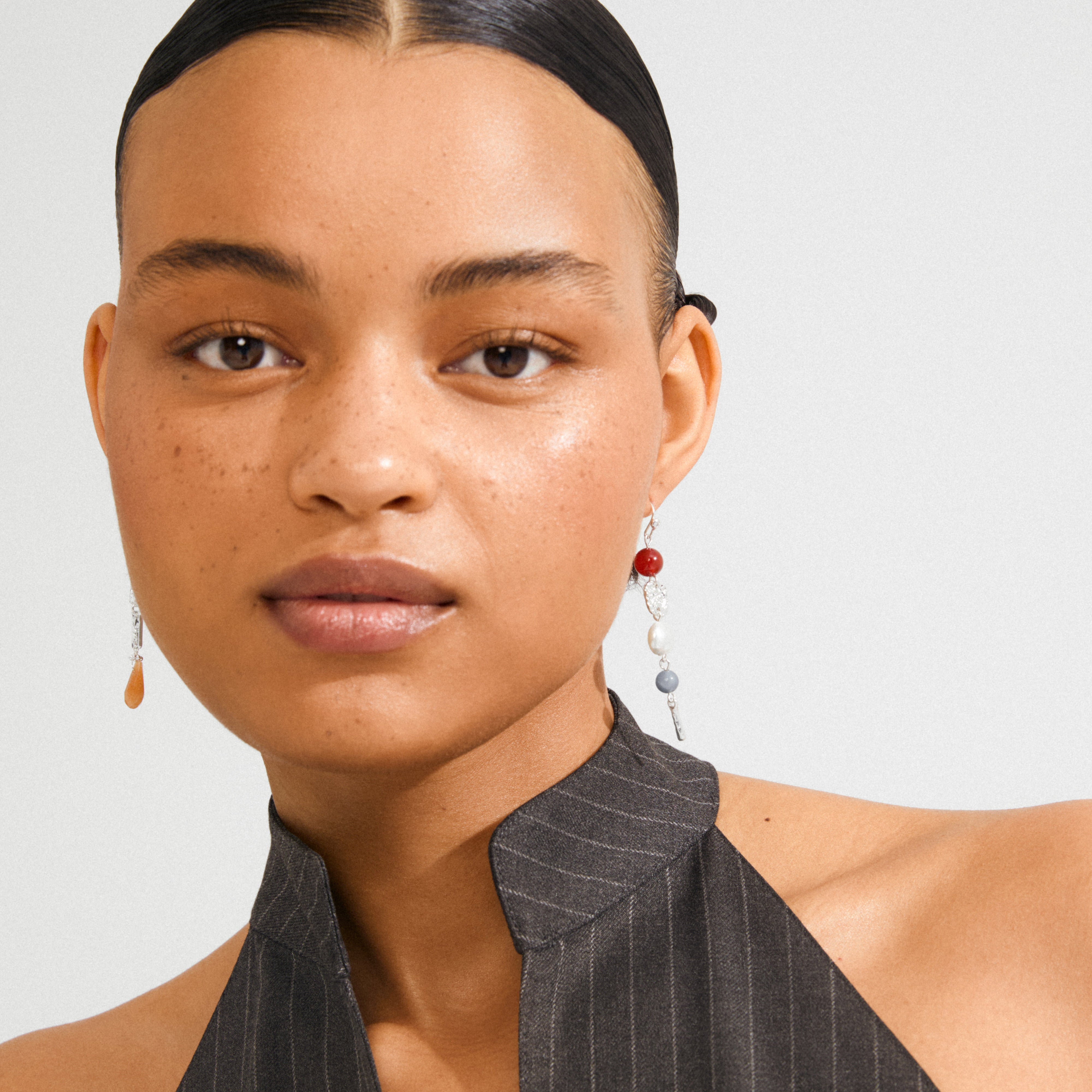 Young woman wearing Pilgrim's SENSE earrings, featuring asymmetrical silver-plated drops with colorful beads, highlighting a boho luxe style.
