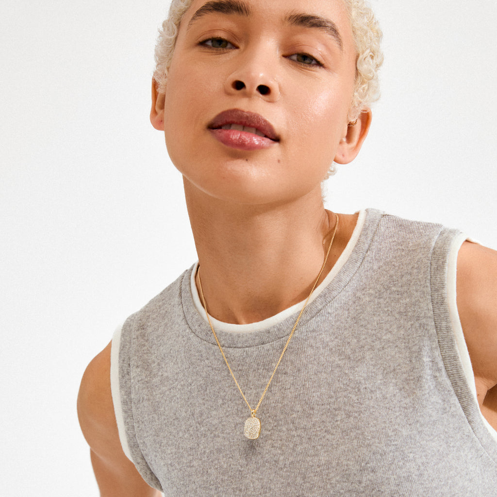 Person wearing EMBER necklace gold-plated by Pilgrim, showcasing a delicate square pavé pendant on a fine chain, reflecting Nordic-inspired, trendy style.