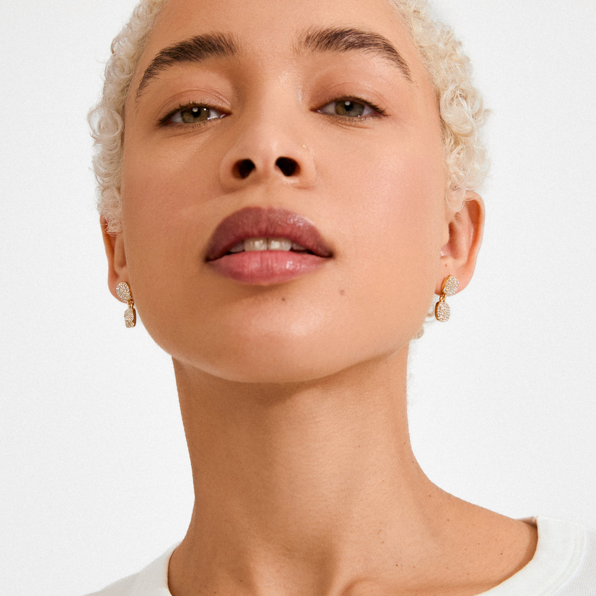 Close-up of a person wearing EMBER earrings gold-plated, showcasing small, gold-tone drop earrings encrusted with sparkling Preciosa crystals, highlighting their elegance and sophistication.