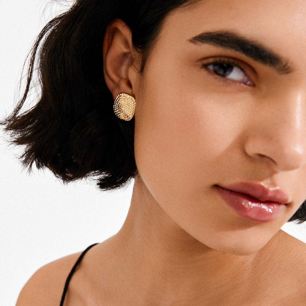 EMBER earrings gold-plated on a woman's ear, featuring a textured square design with raised dots, showcased against a minimalist white background.