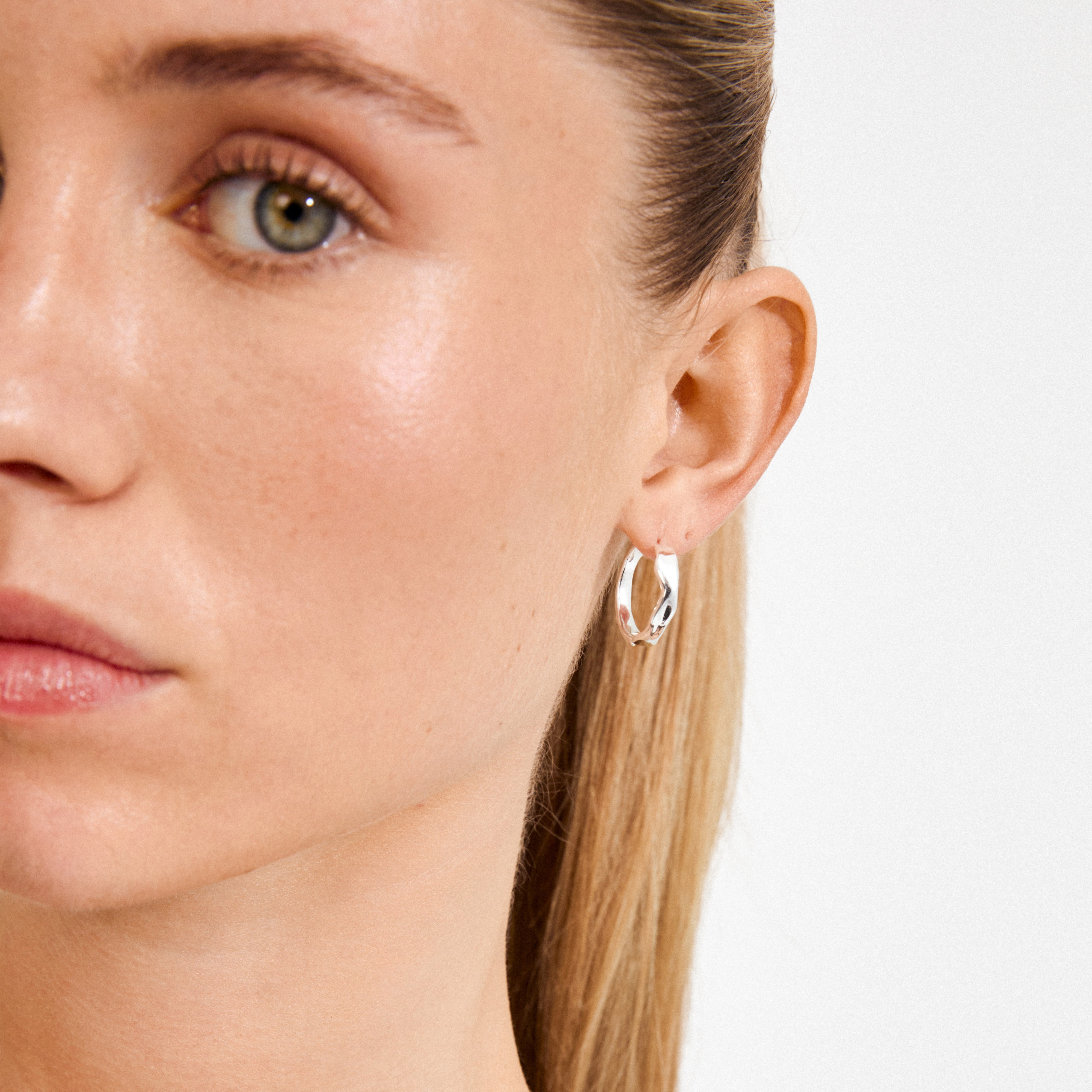 EMBER hoop earrings silver-plated on a woman's ear, showcasing their wavy, sculptural design. Hair pulled back highlights the earring's modern, effortless style.