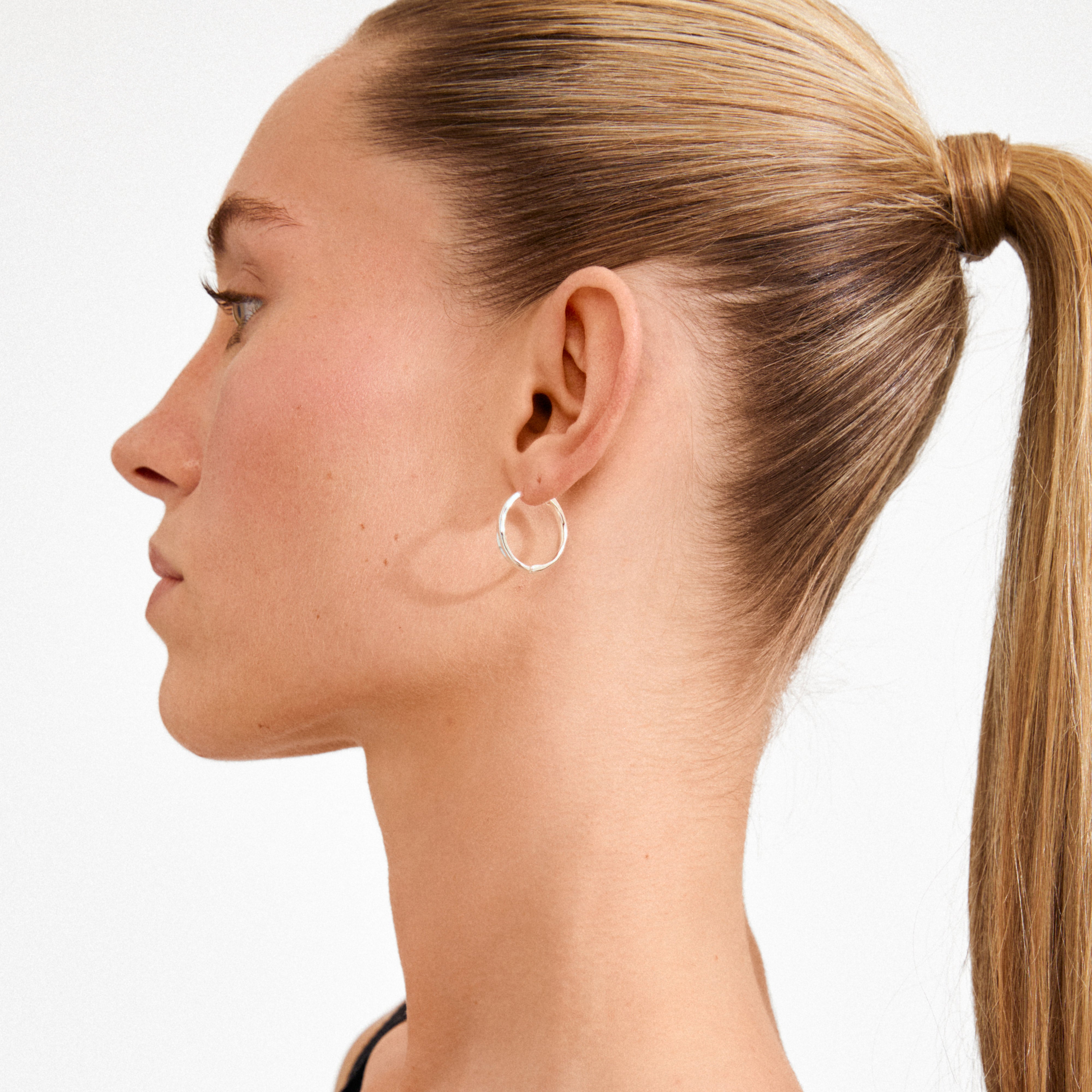 Close-up of a young person wearing EMBER silver-plated hoop earrings with sculptural curves, showcasing a sleek, modern design.