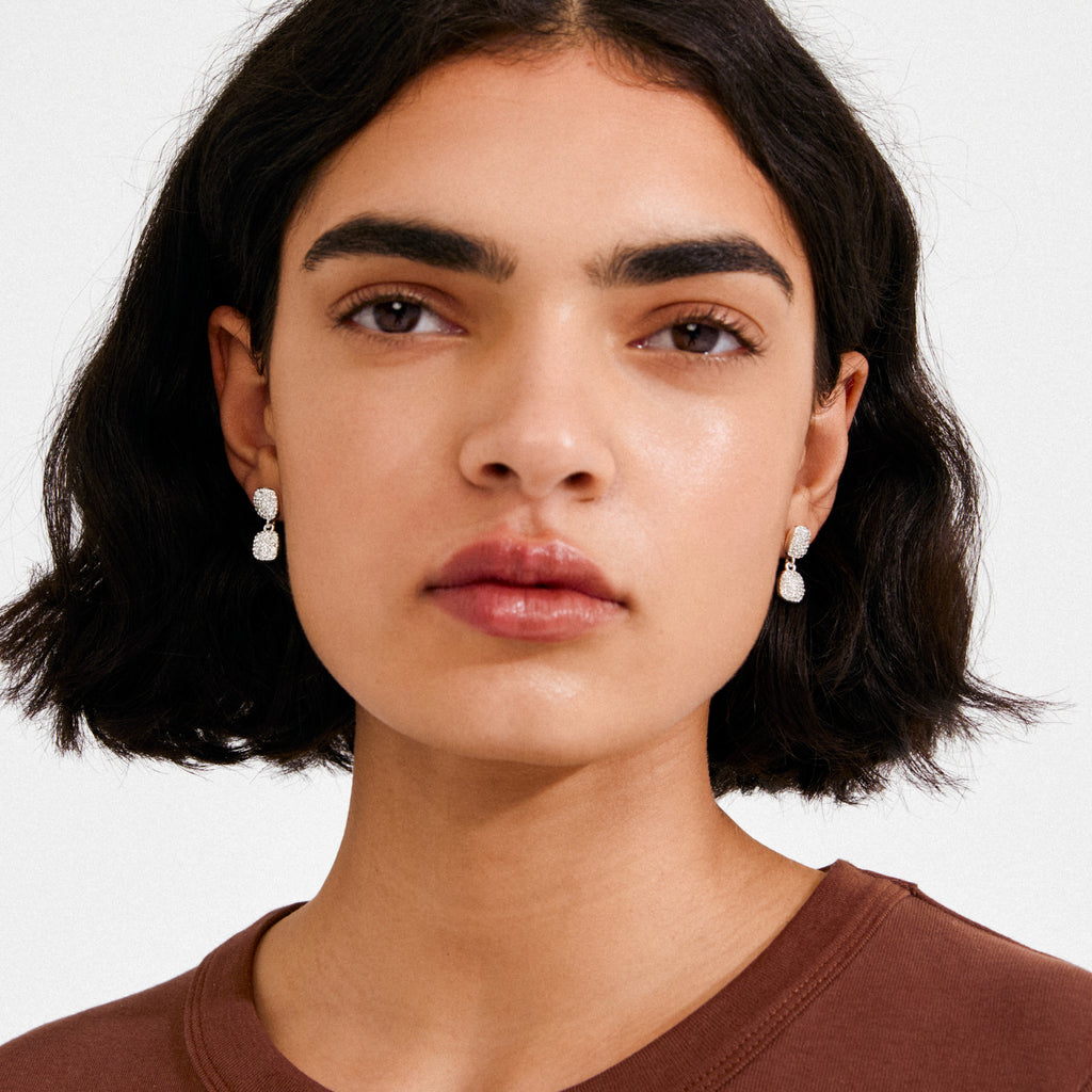 Young woman models EMBER earrings, silver-plated with pavé-set crystals, showcasing Pilgrim's blend of timeless elegance and modern style against a plain backdrop.
