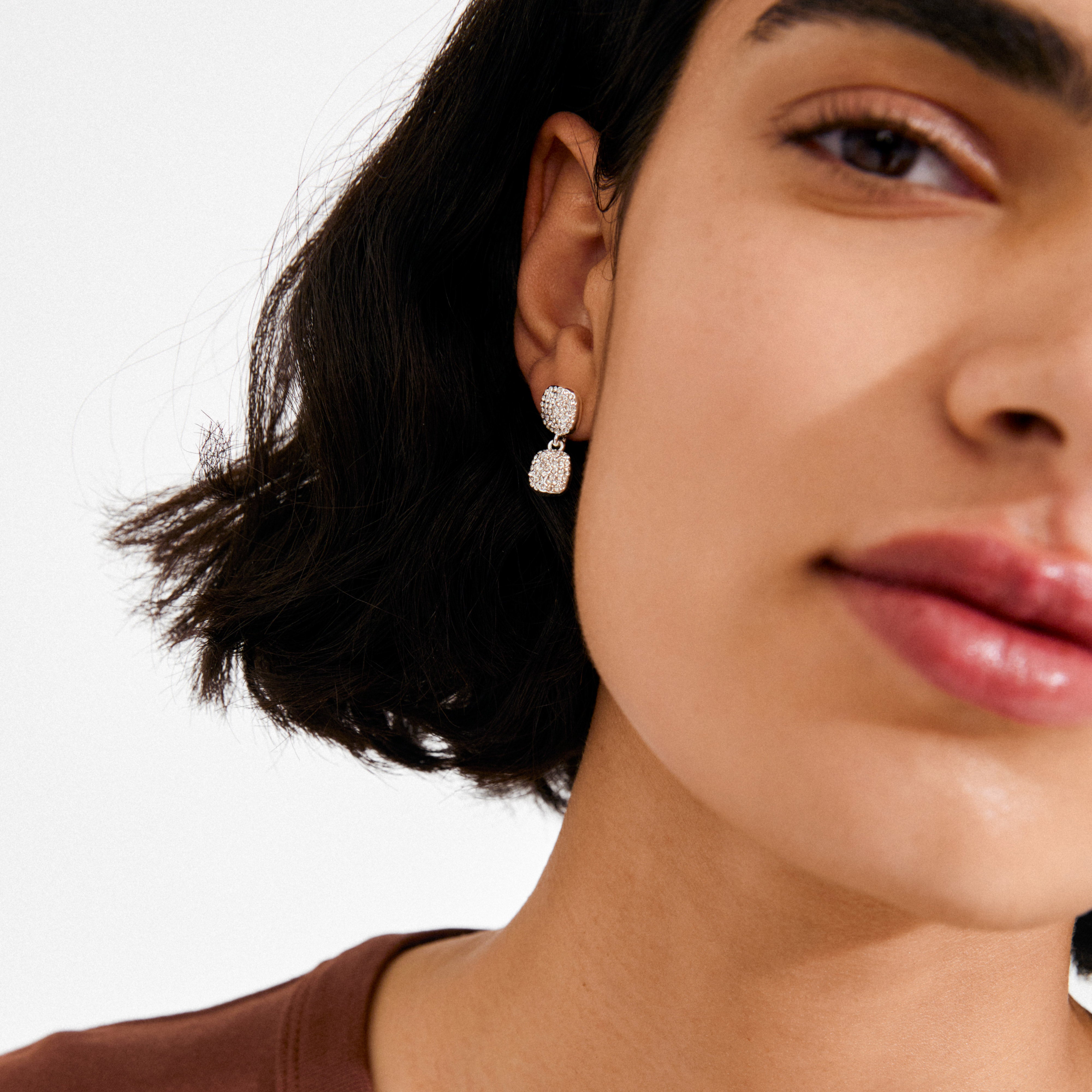 Young woman wearing Pilgrim's EMBER silver-plated earrings with dual square crystal drops, highlighting a blend of elegance and sparkle against a minimalist style.