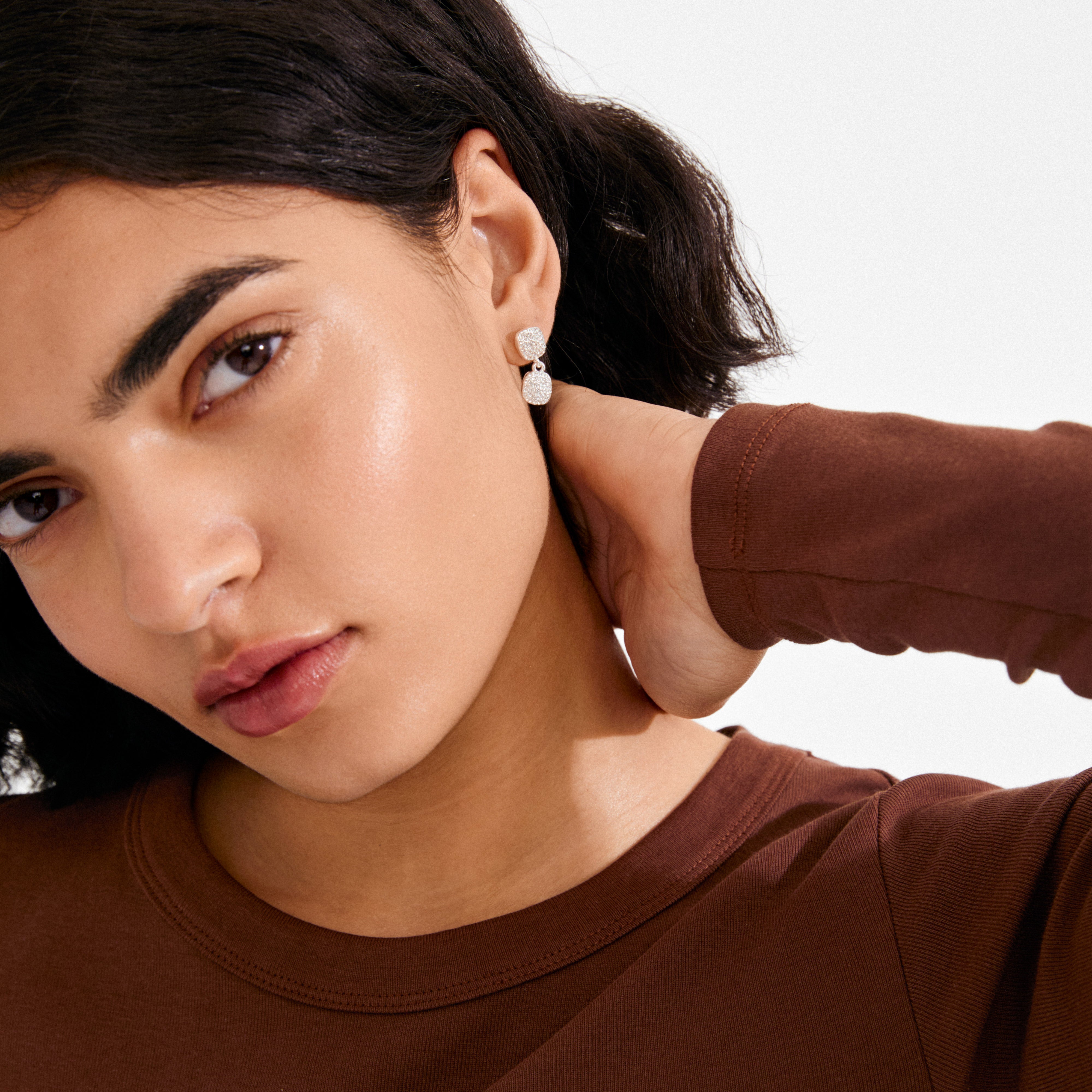 Young woman with dark hair showcases Pilgrim's EMBER earrings, featuring silver-plated drop design with sparkling stones, highlighting a sophisticated, effortless style.
