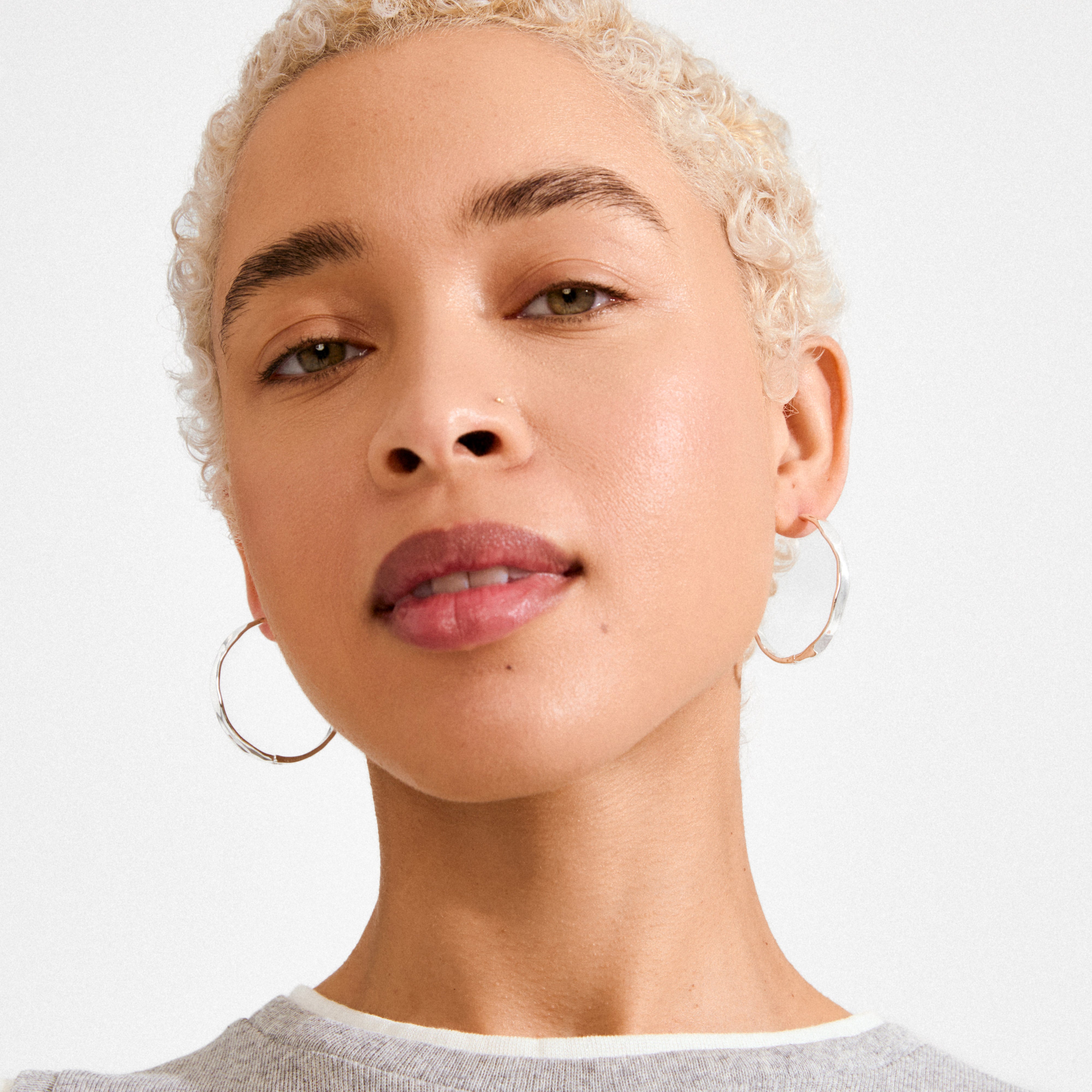 Close-up of a person wearing Pilgrim's silver-plated EMBER hoop earrings, showcasing their subtle wavy design for versatile, day-to-night style.
