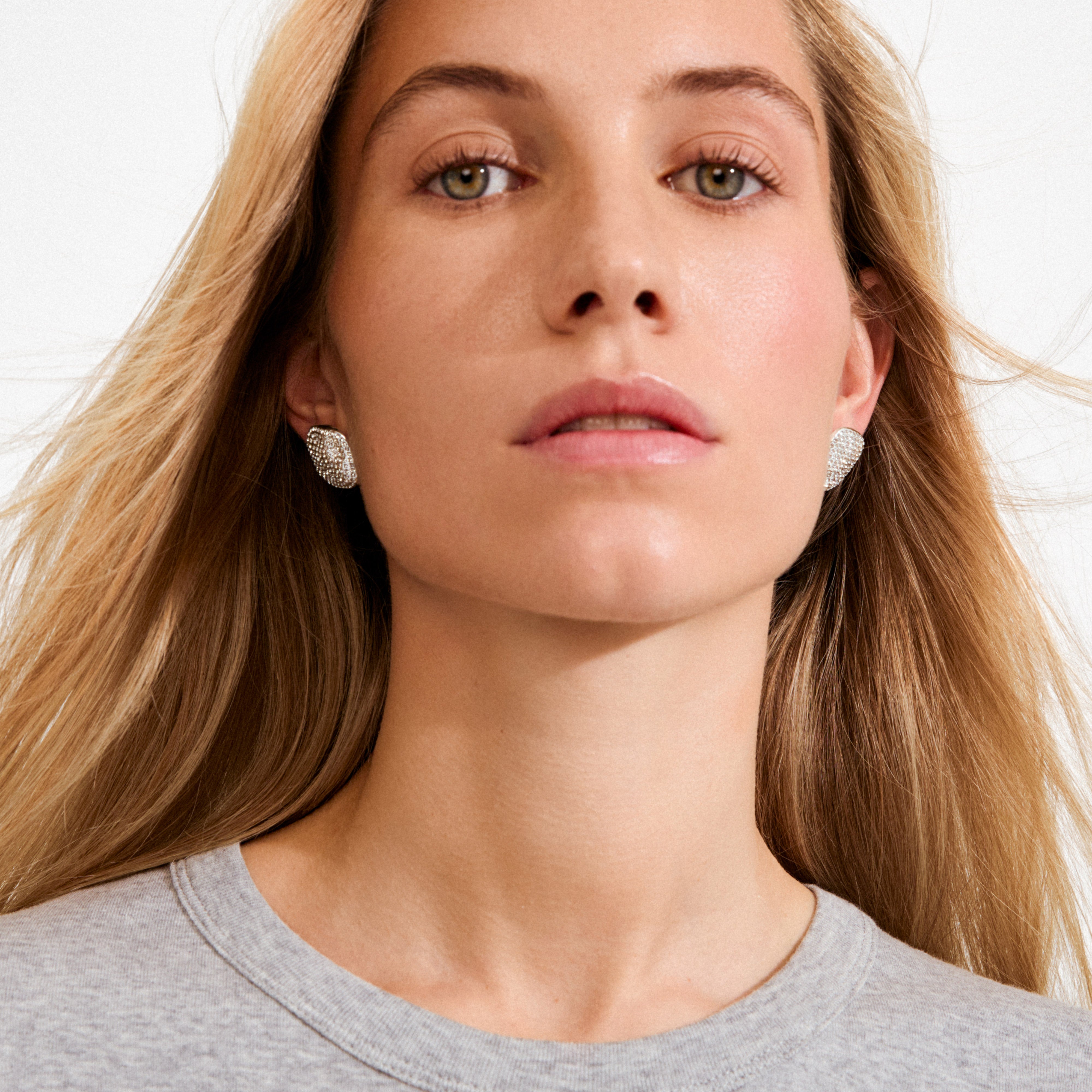 Young woman wearing Pilgrim's EMBER silver-plated stud earrings with sparkling crystals, showcasing an elegant square design against a softly lit background.