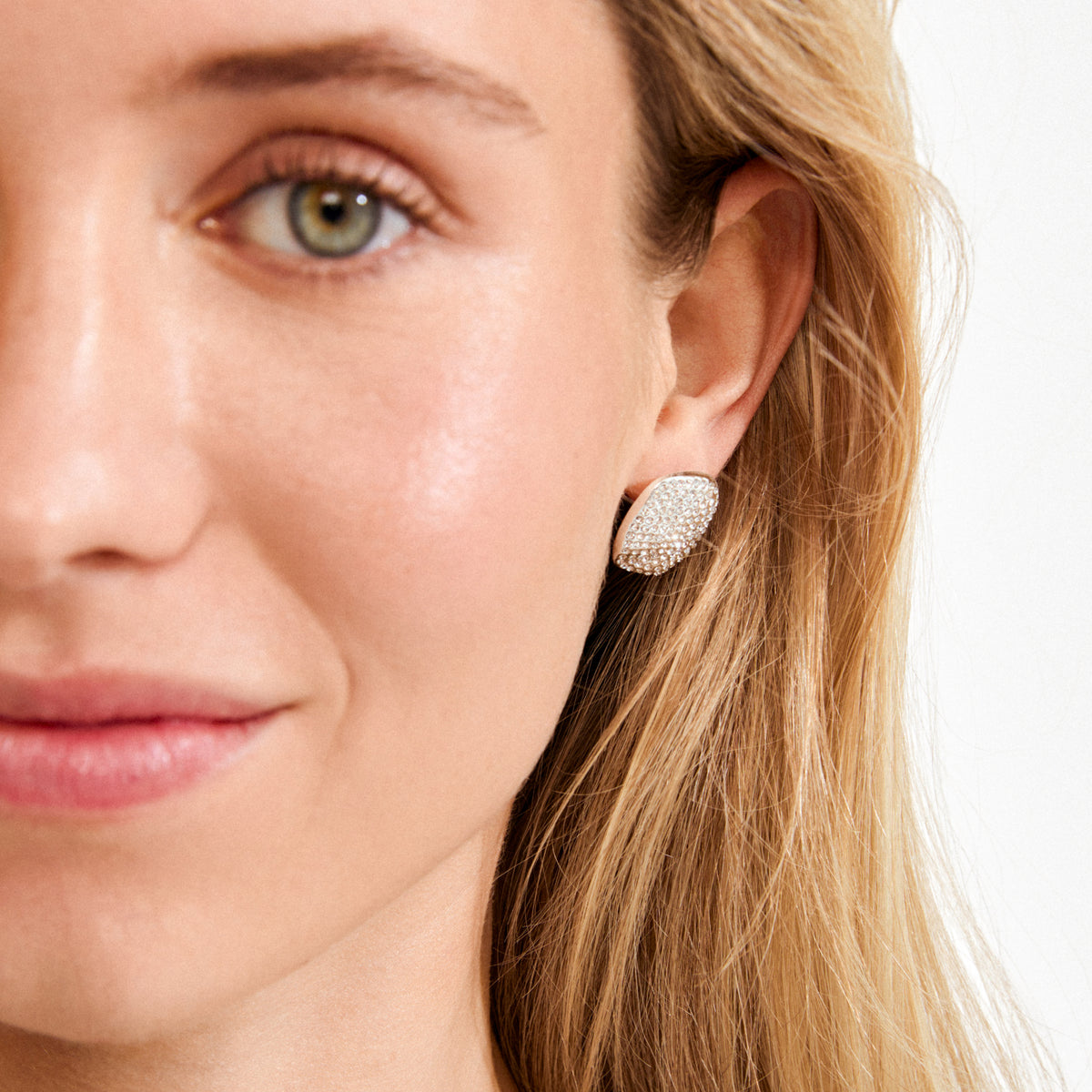 Close-up of a woman wearing Pilgrim's EMBER earrings, silver-plated with sparkling pavé Preciosa crystals, showcasing a luxurious, soft square design on her ear.