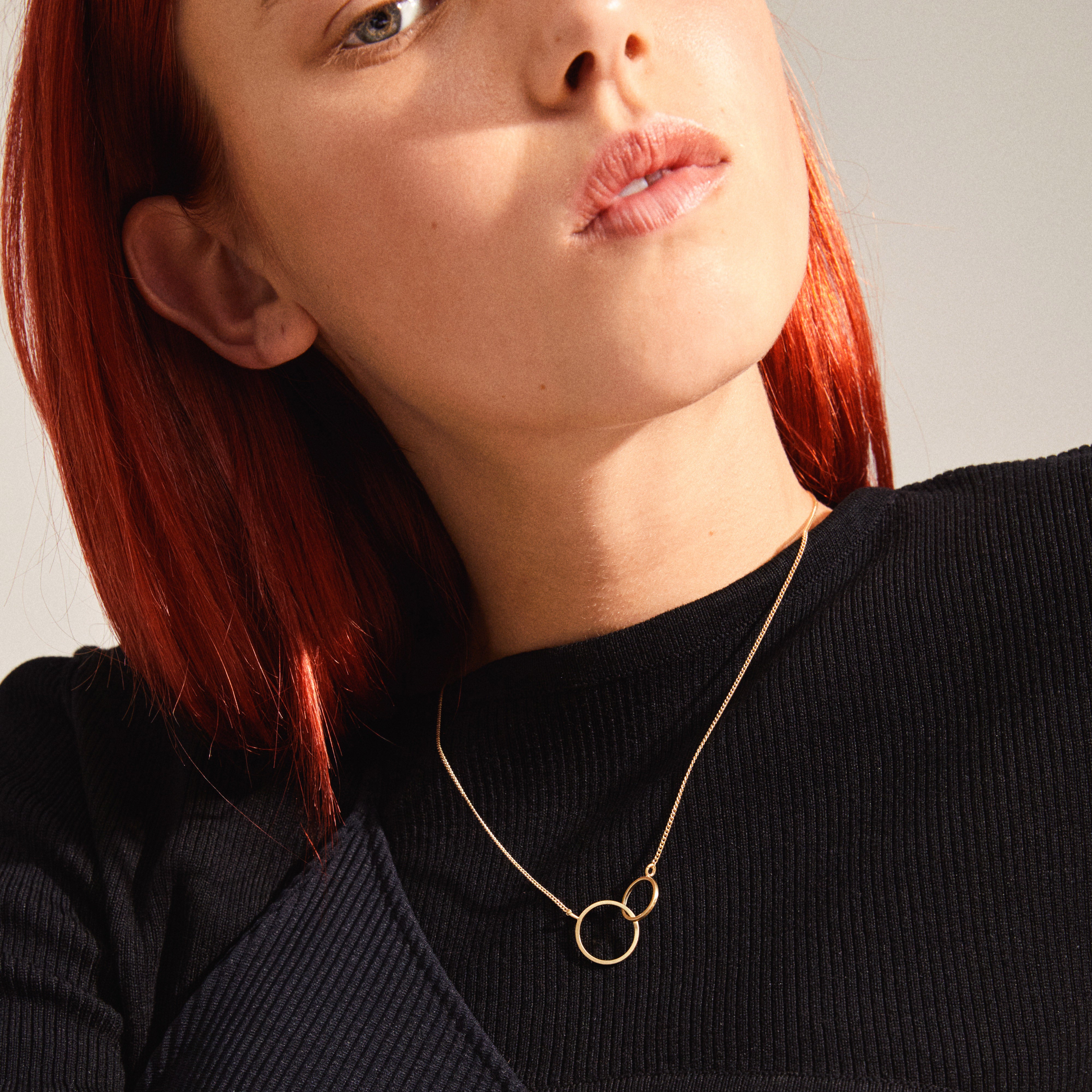 HARPER necklace gold-plated featuring two intertwined rings, worn by a woman with red hair, showcasing its elegant design and symbolic connection.