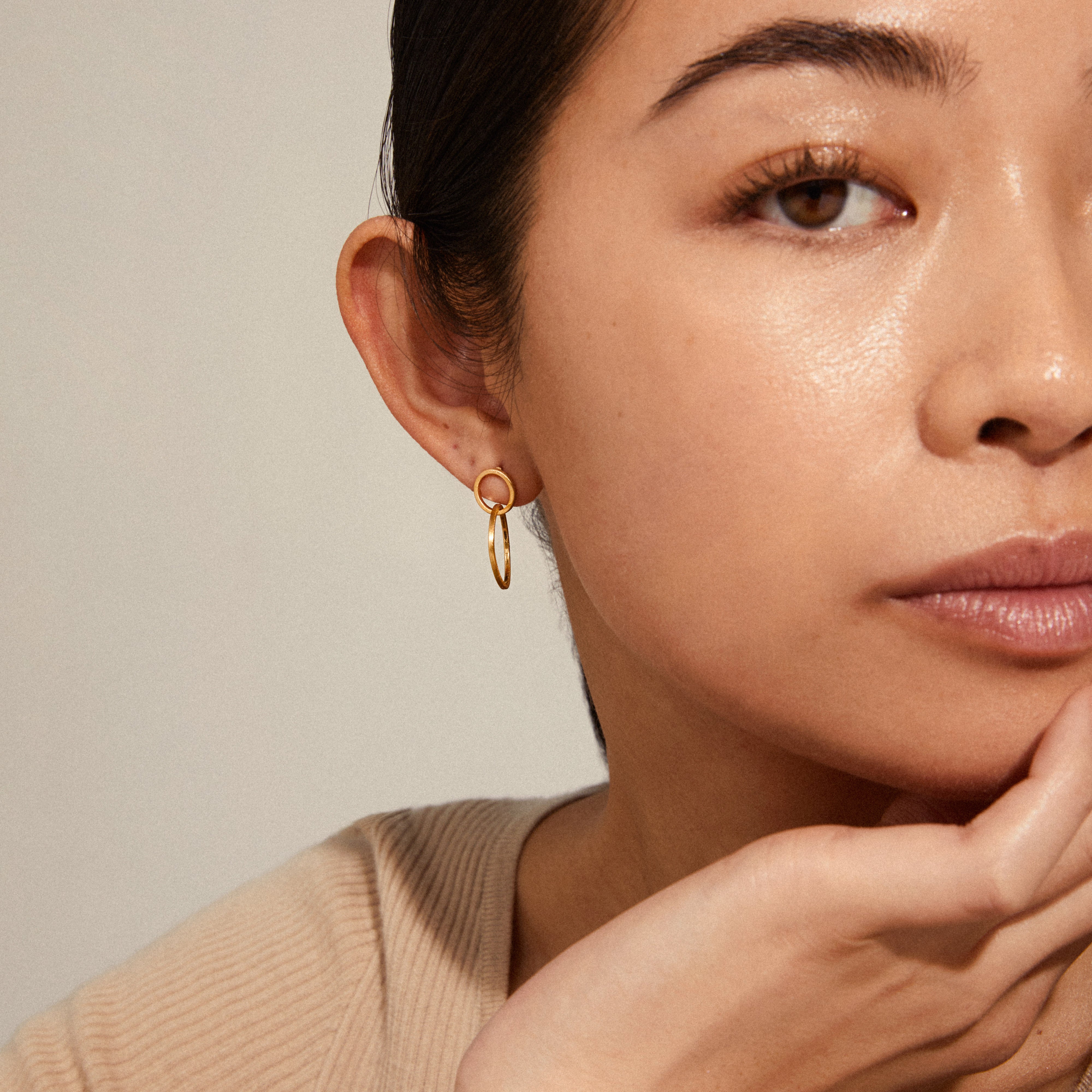 HARPER gold-plated earrings featuring two intertwined satin-matte rings, elegantly showcased by a woman touching her chin, embodying Nordic design tradition.