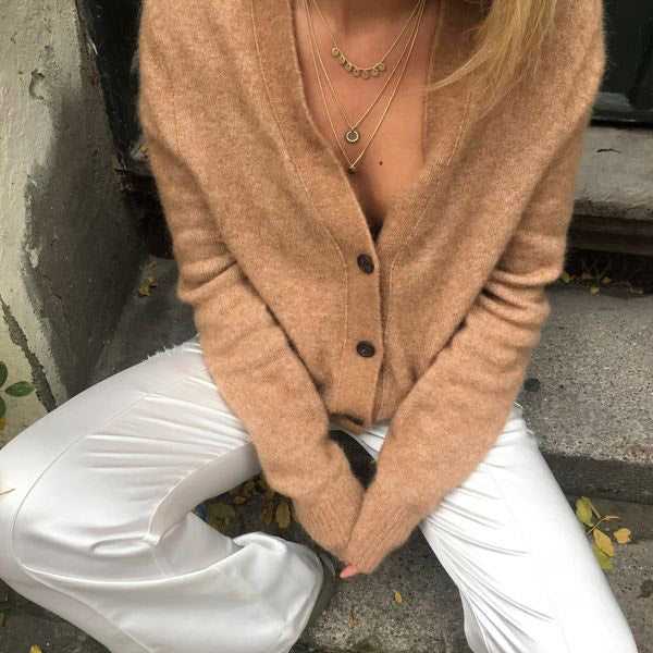 Person wearing the ARDEN 3-in-1 crystal necklace, gold-plated, with layered amulets and crystals, adding a unique, feminine touch to their outfit on outdoor steps.