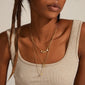 Dark-skinned person wearing the ARDEN 3-in-1 crystal necklace gold-plated, featuring layered gold chains with textured pendants and charms, elegantly displayed on a rib-knit tank top.