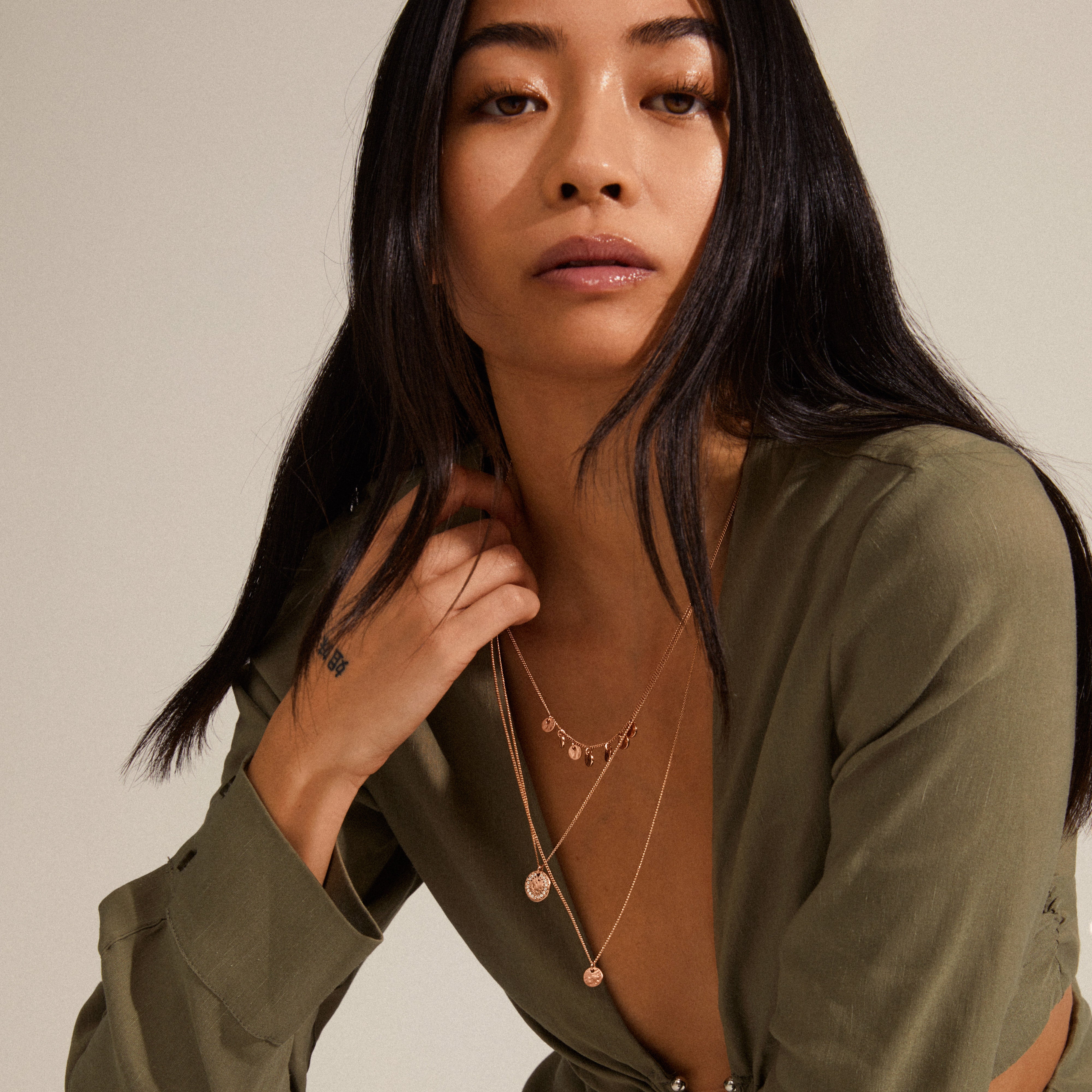 Young woman wears the ARDEN 3-in-1 crystal necklace in rosegold, featuring layered gold chains with disc charms and a round pendant, styled with an olive blouse.