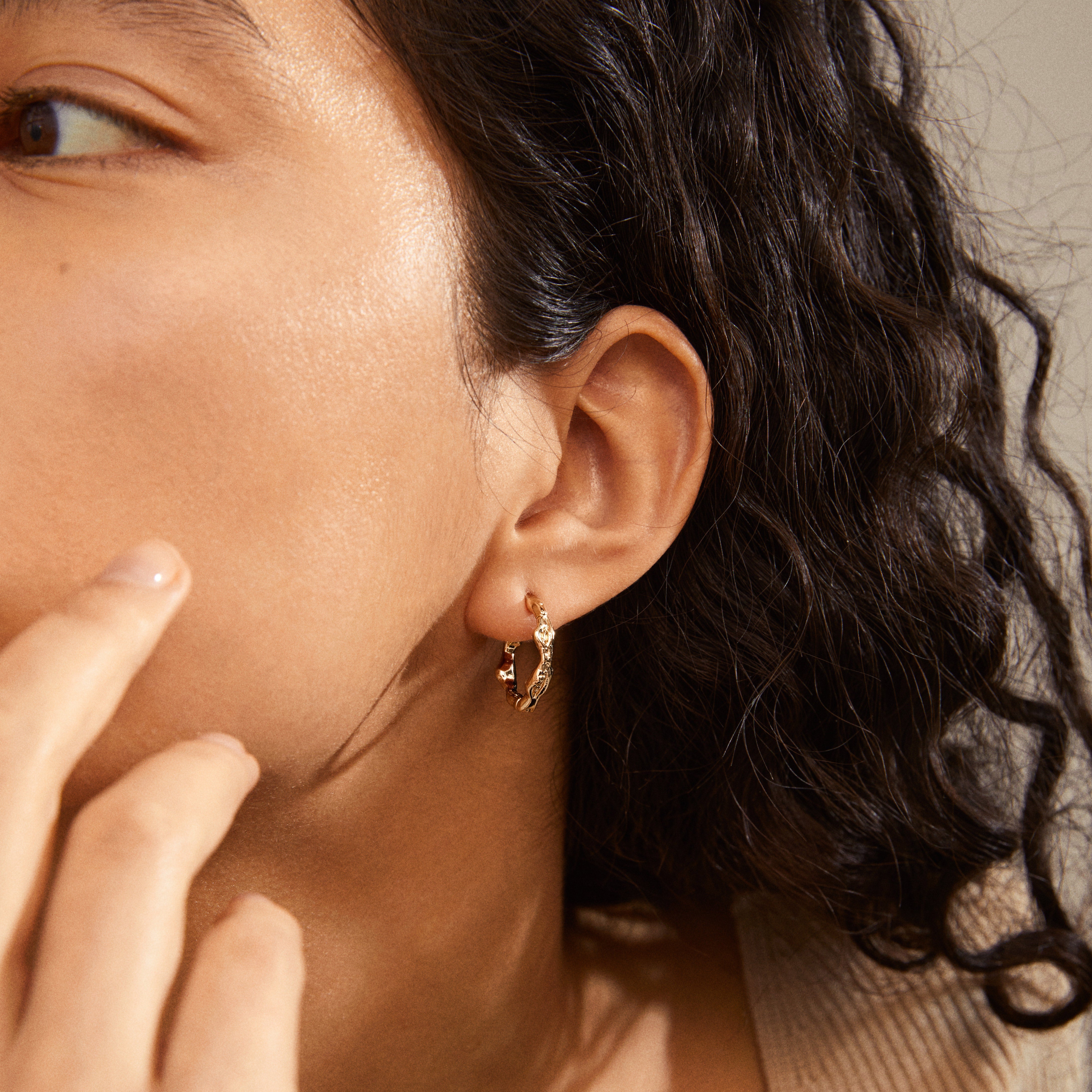 Close-up of a woman's ear wearing Pilgrim's ZION organic-shaped medium hoops, gold-plated, showcasing nature-inspired elegance and a unique boho-chic design.