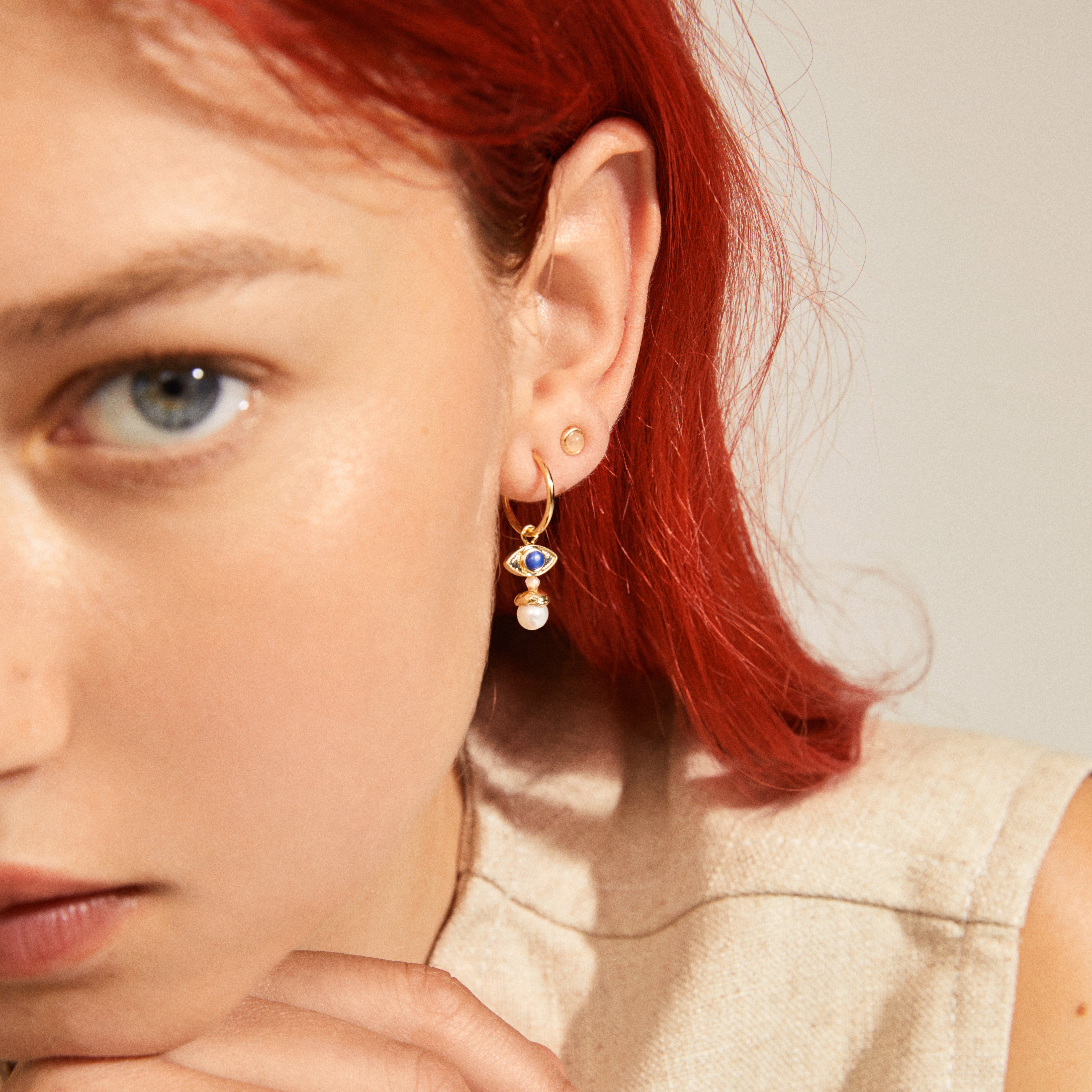 THANKFUL asymmetric 2-in-1 set earrings gold-plated featuring quirky semi-hoops with eye pendants and freshwater pearls, worn by a red-haired woman.