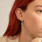 Close-up of a woman wearing THANKFUL asymmetric 2-in-1 gold-plated earrings, featuring a pearl and eye pendant, showcasing their playful, trendy design.