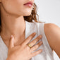 Woman's hand wearing the BLOSSOM organic-shaped gold-plated ring, featuring an irregular silhouette, resting on her chest with a light gray sleeveless top visible.