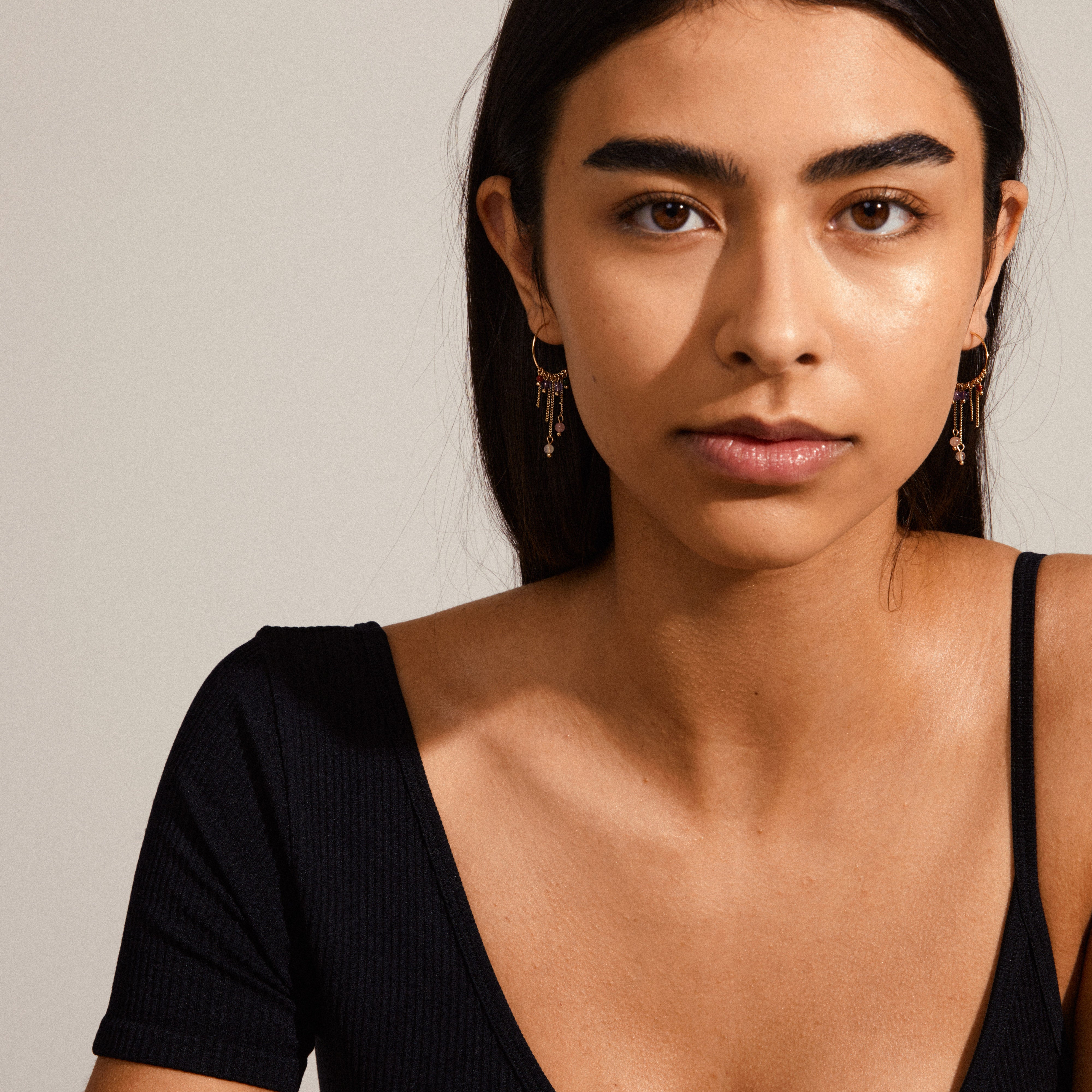 Woman wearing PEACE semi-precious stone hoop earrings, gold-plated, featuring asymmetrical pendants and colorful stones, exuding a luxurious boho look.