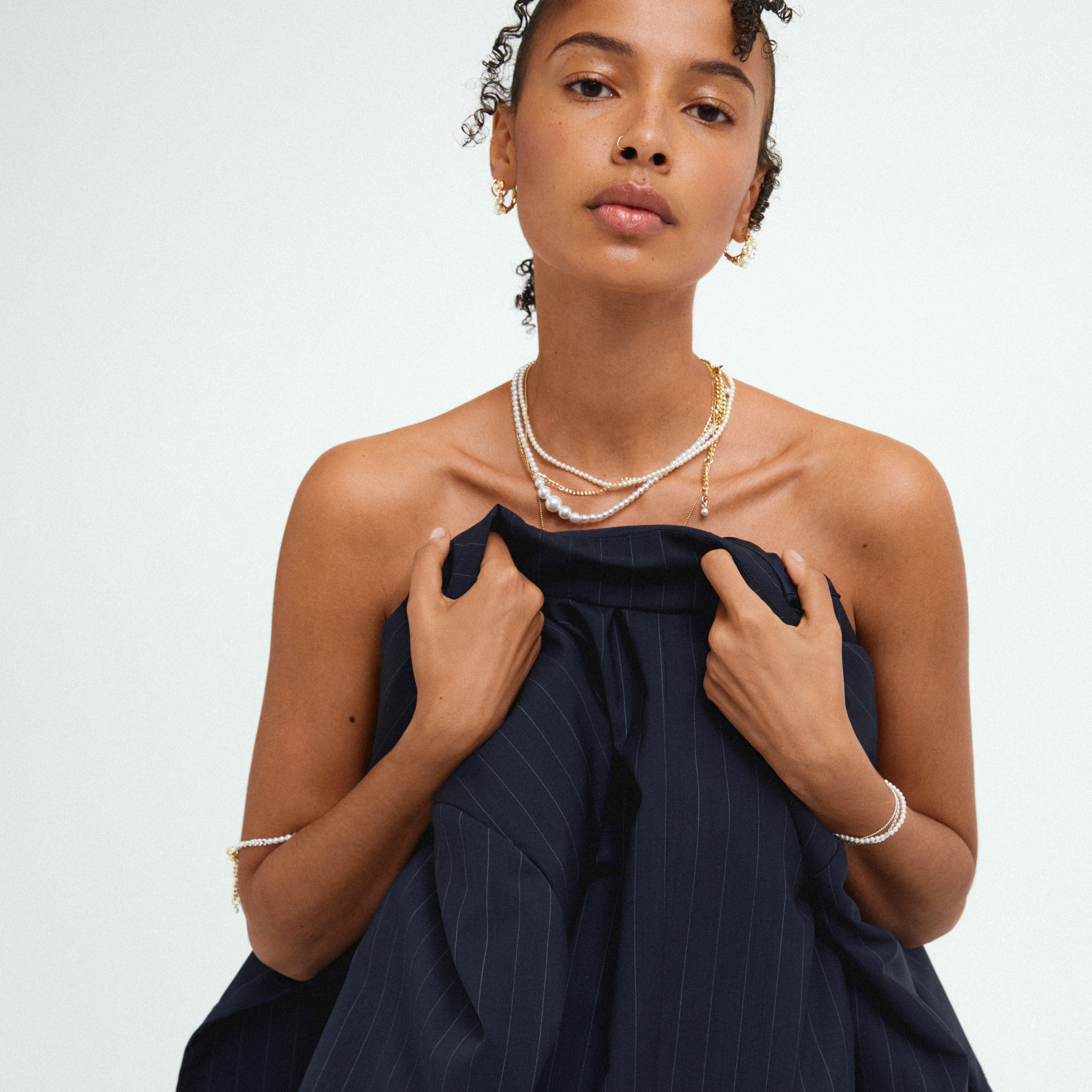 Woman showcasing BEAT pearl necklace gold-plated, featuring an elegant asymmetrical design with a curb chain and pearls, embodying empowerment and versatile style.