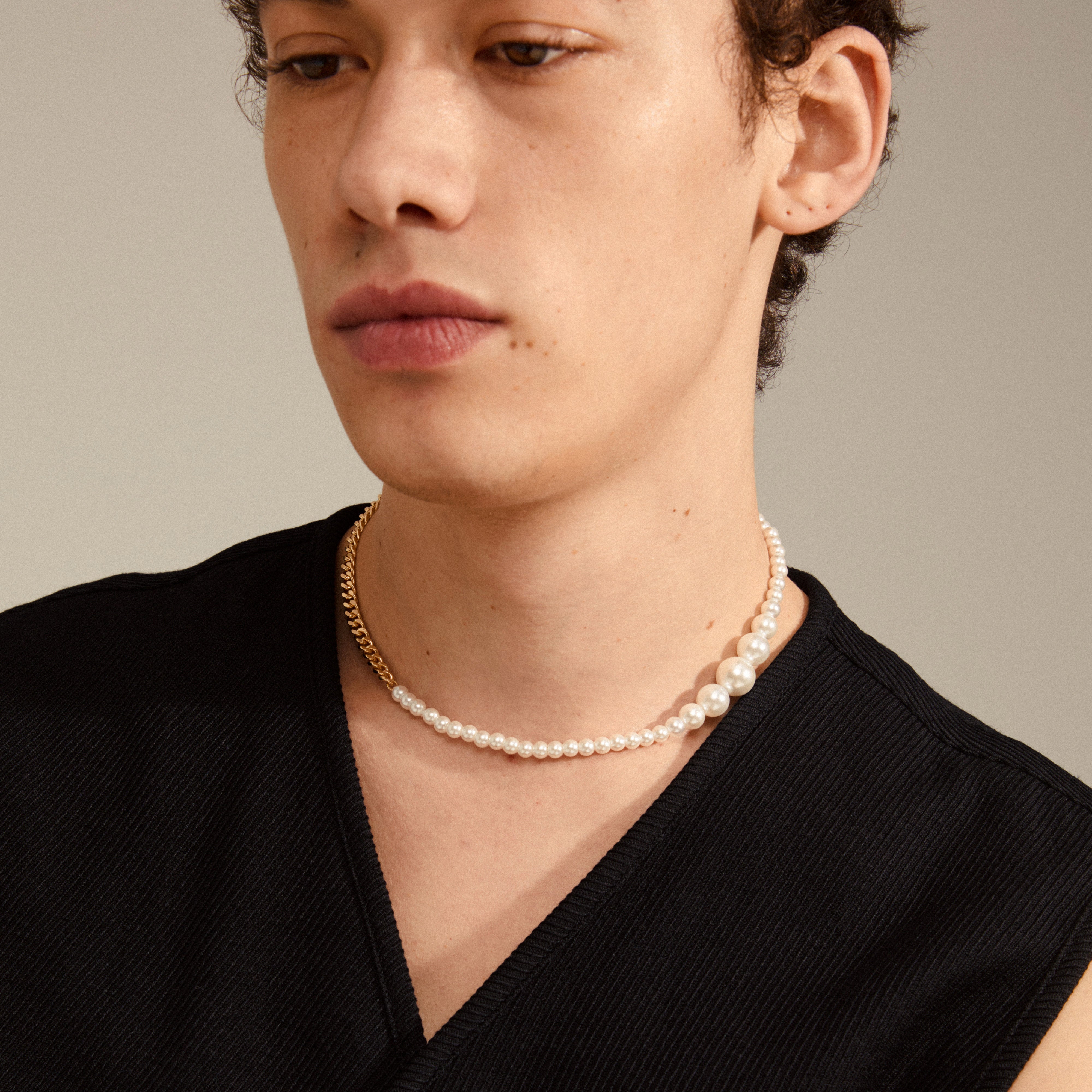 Person wearing the BEAT pearl necklace gold-plated, featuring an asymmetrical blend of pearls and gold-plated curb chain, epitomizing empowerment and urban style.