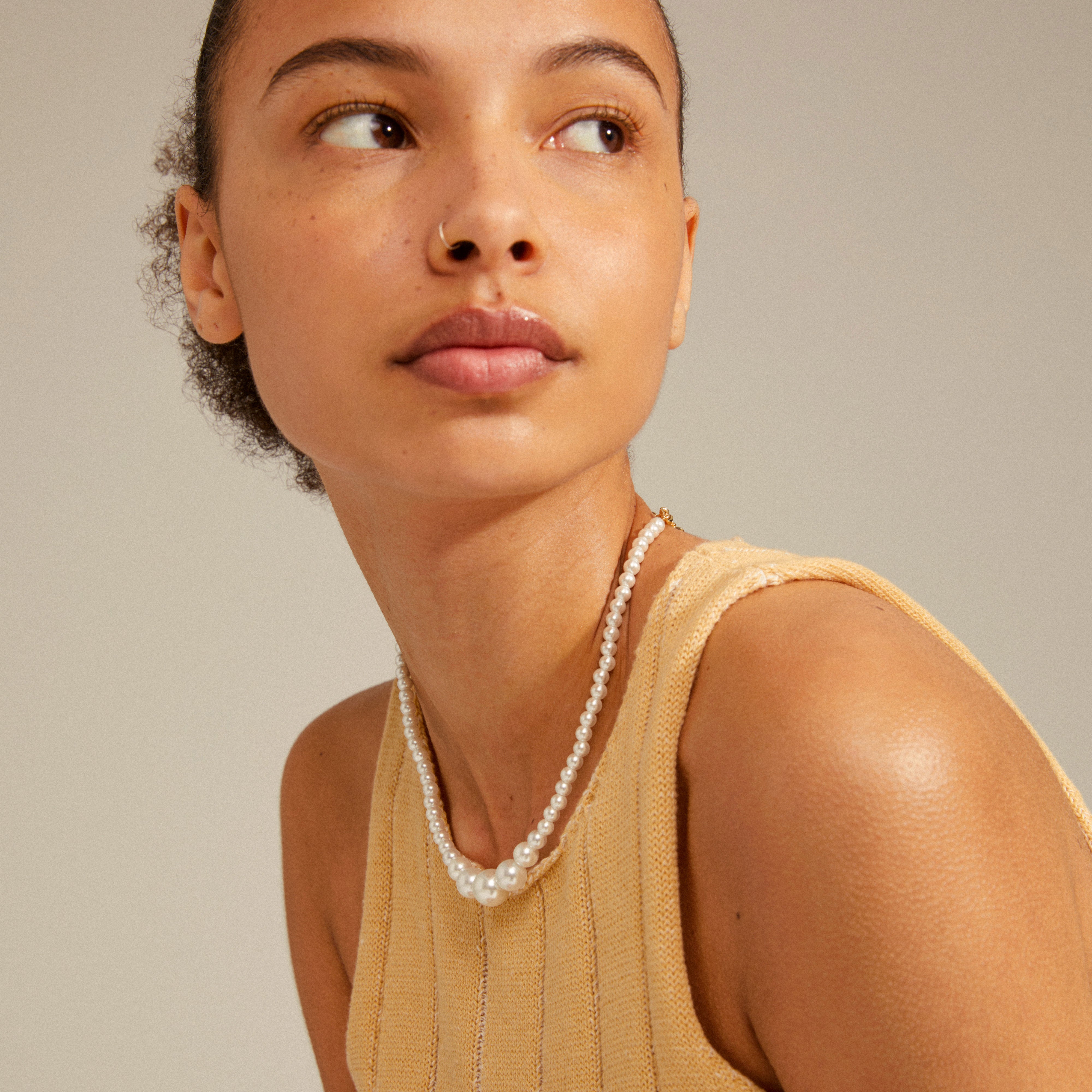 Close-up of a woman wearing the BEAT pearl necklace, featuring an asymmetrical gold-plated curb chain and pearls, embodying empowerment and urban elegance.