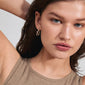 Gold-plated CONNECT crystal earrings with wavy oval hoops, featuring shiny Preciosa crystals and a click clasp. Model showcases the earrings in a styled pose.