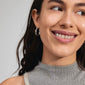 Woman smiling wearing CONNECT crystal earrings, silver-plated with wavy design and Preciosa crystals, symbolizing love and kindness from Pilgrim.