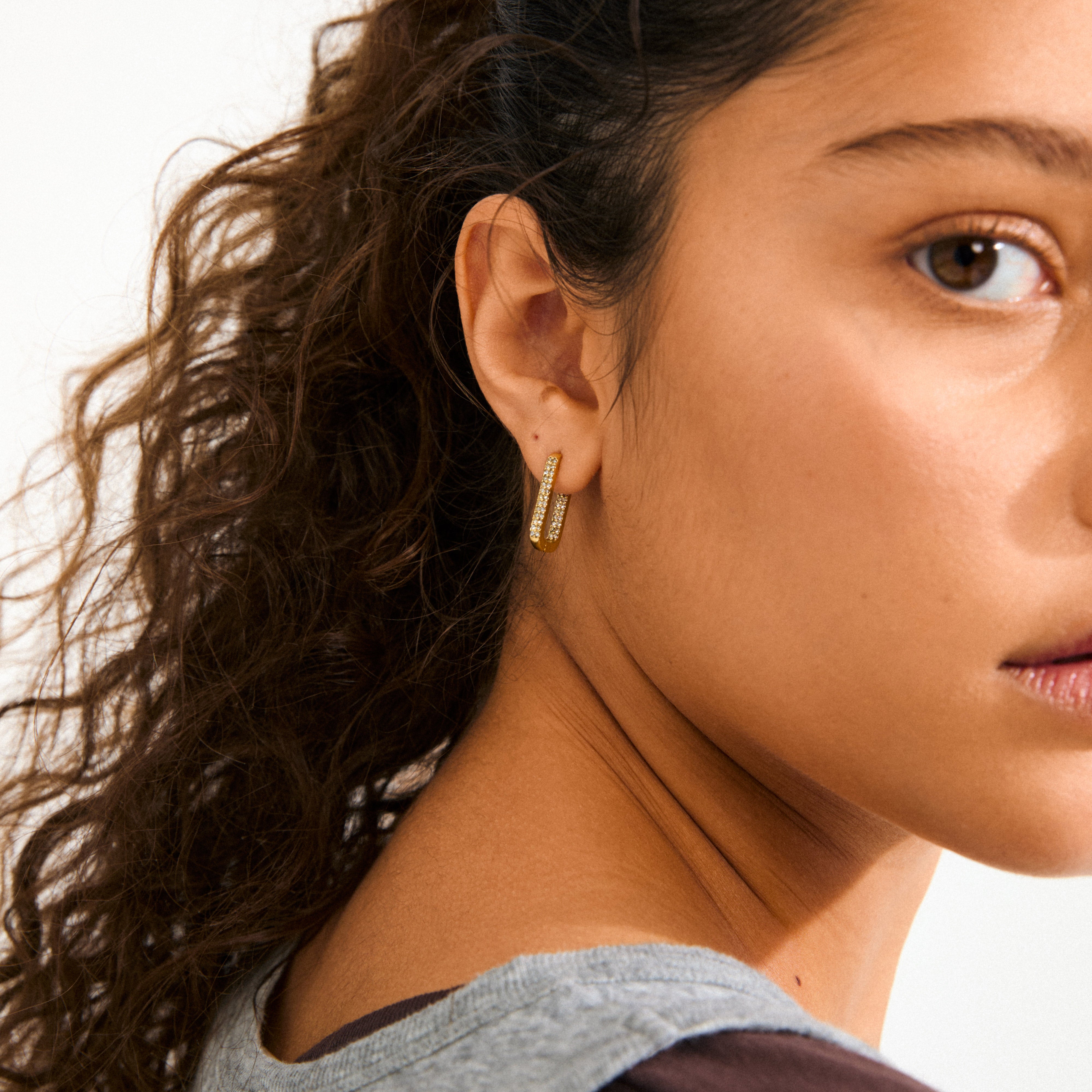 Side view of a young person wearing Pilgrim's PHASE oval hoops gold-plated earrings, featuring parallel bars with sparkling stones, highlighting Scandinavian elegance and sustainable craftsmanship.