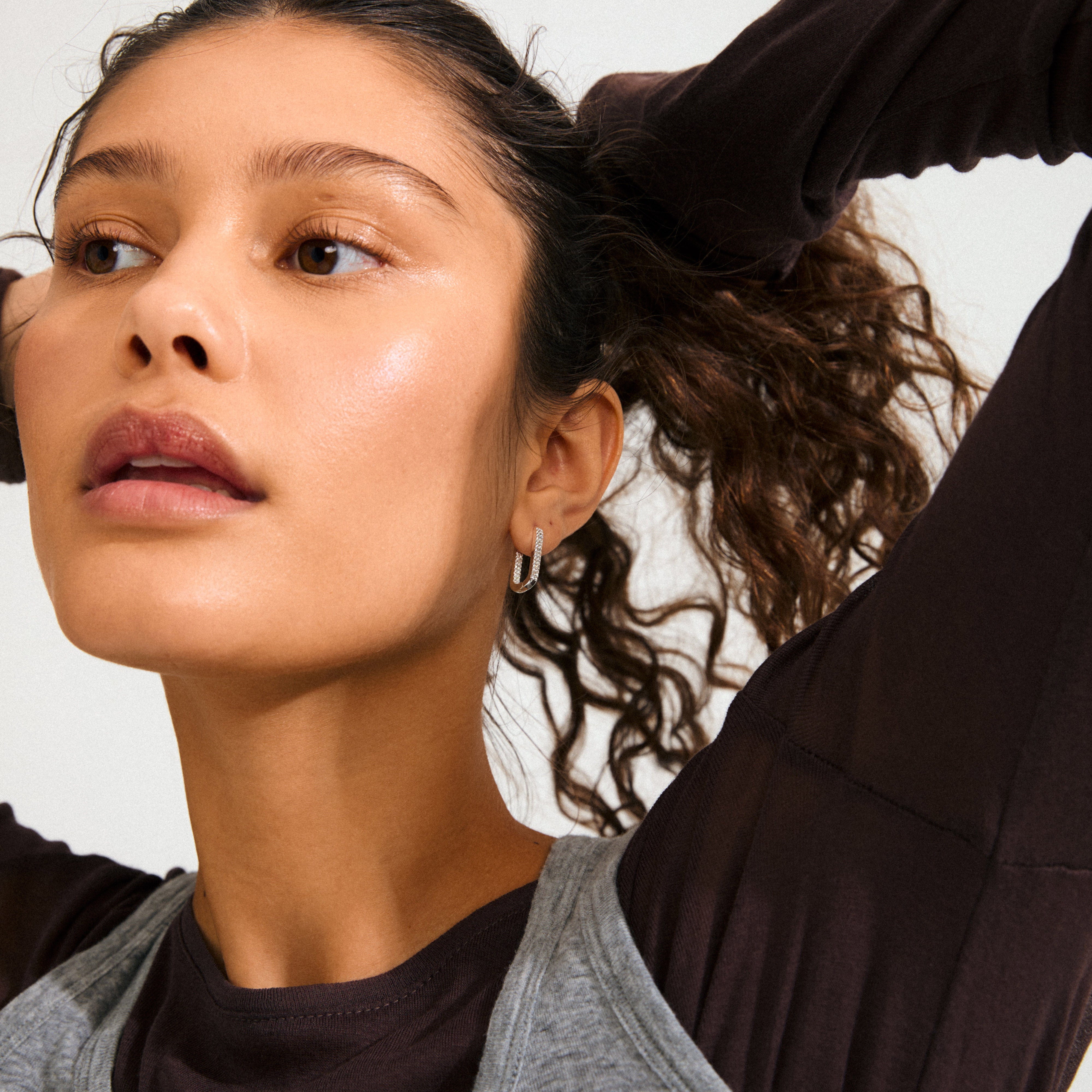 Young person wears PHASE oval hoops silver-plated earring by Pilgrim, featuring sparkling Preciosa crystals. Their raised arms highlight the earring's elegant design and craftsmanship.