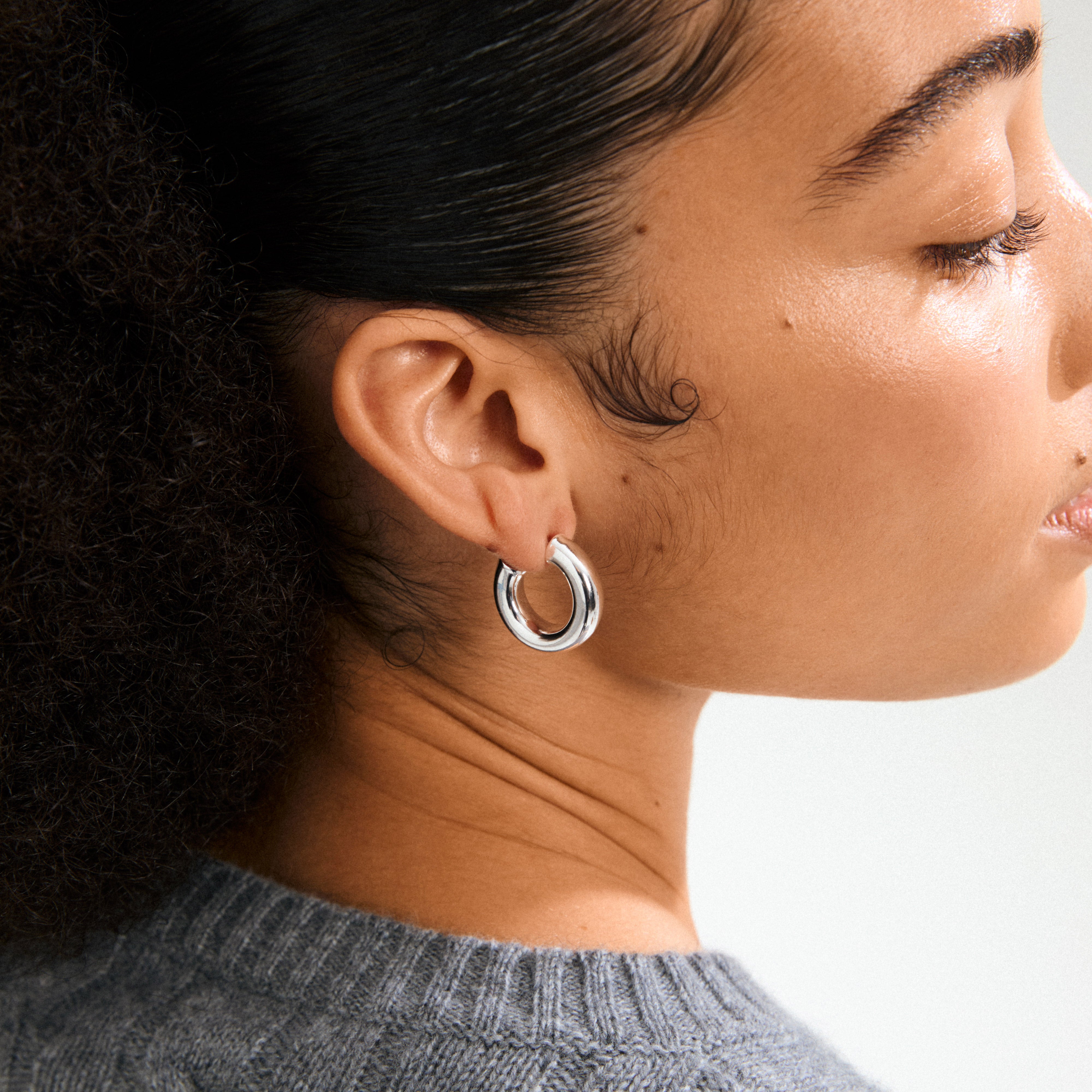Side-profile close-up of a person wearing PHASE large hoops silver-plated earrings, showcasing their chunky, refined design, paired with a knit sweater.